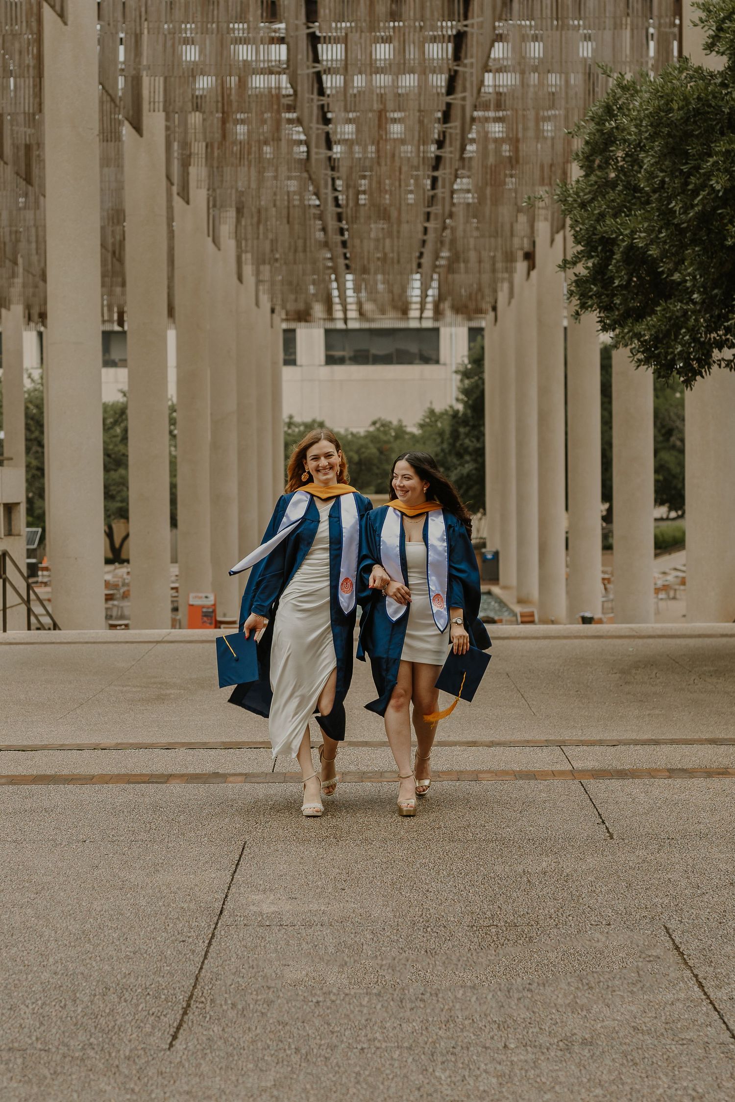 Two friends walking together under modern architectural columns in casual attire.