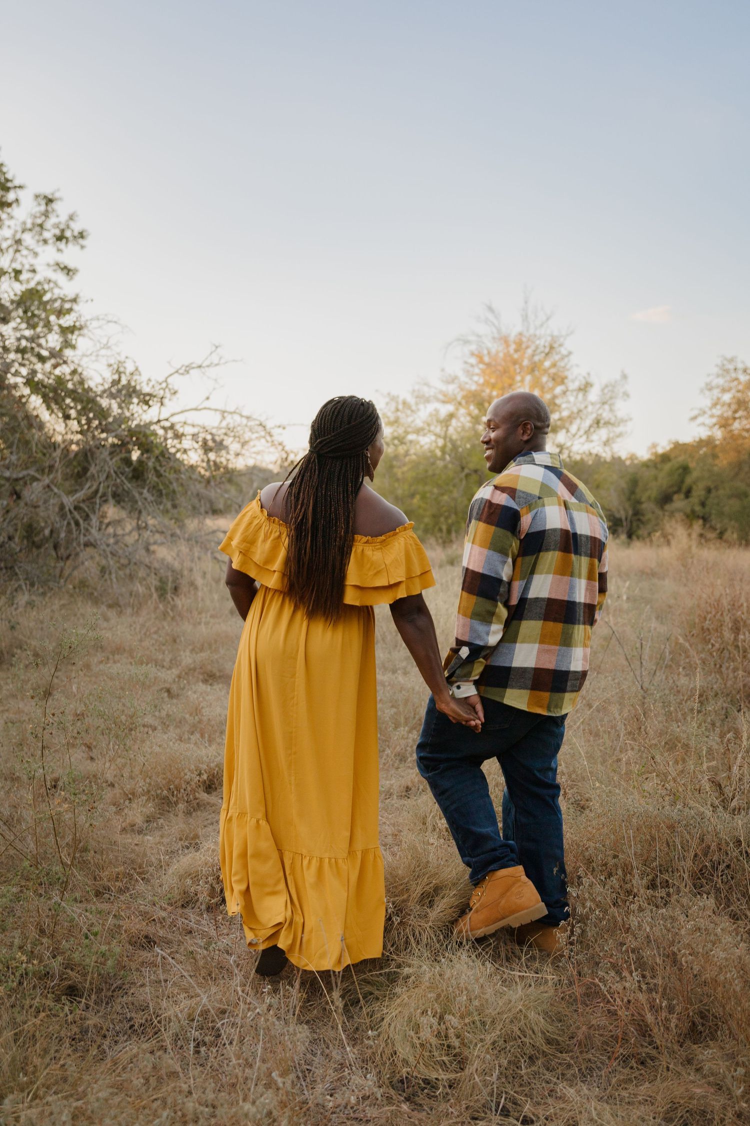 Couple holding hands while walking through golden field at sunset.