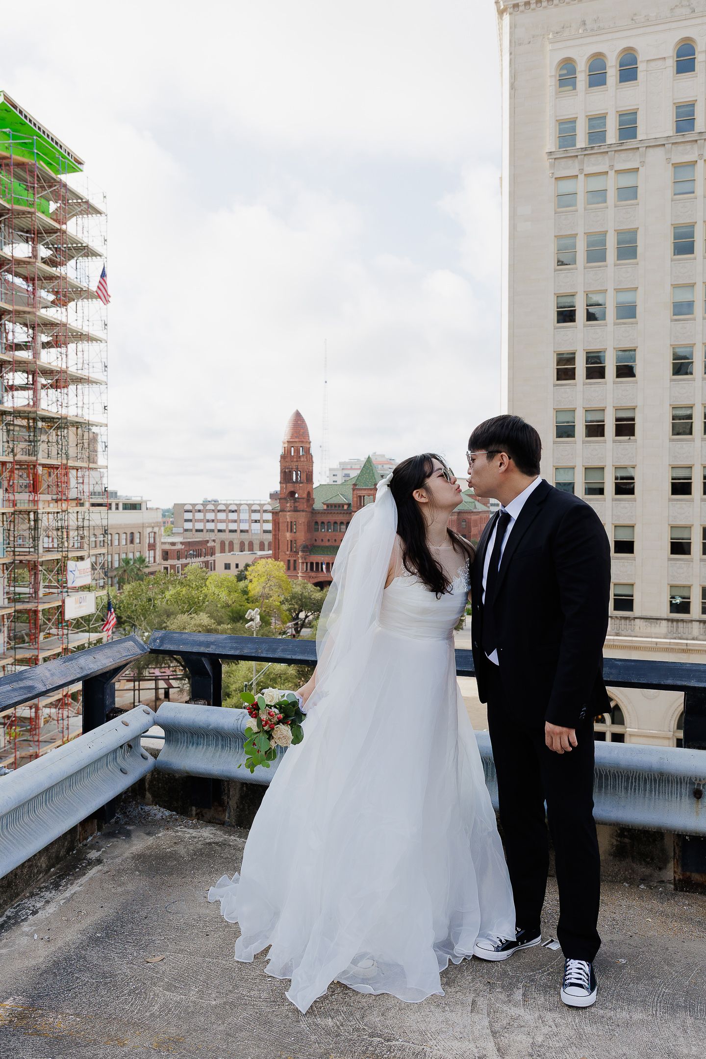 A bride and groom share romantic moments on a rooftop with city buildings and scaffolding in the background.