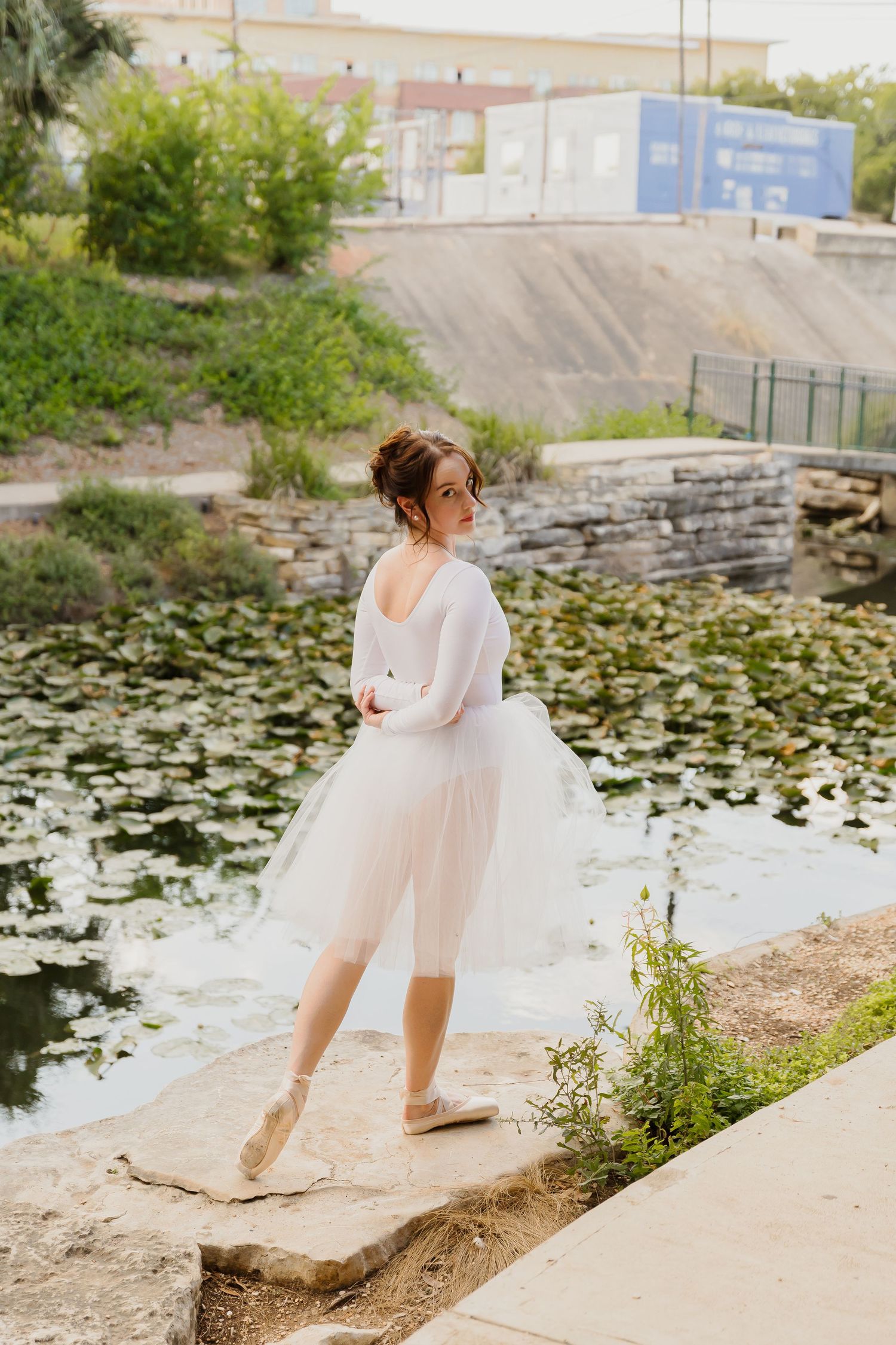 Young ballet dancer in pink tutu dress performs graceful poses by a serene lily pond on a summer day.