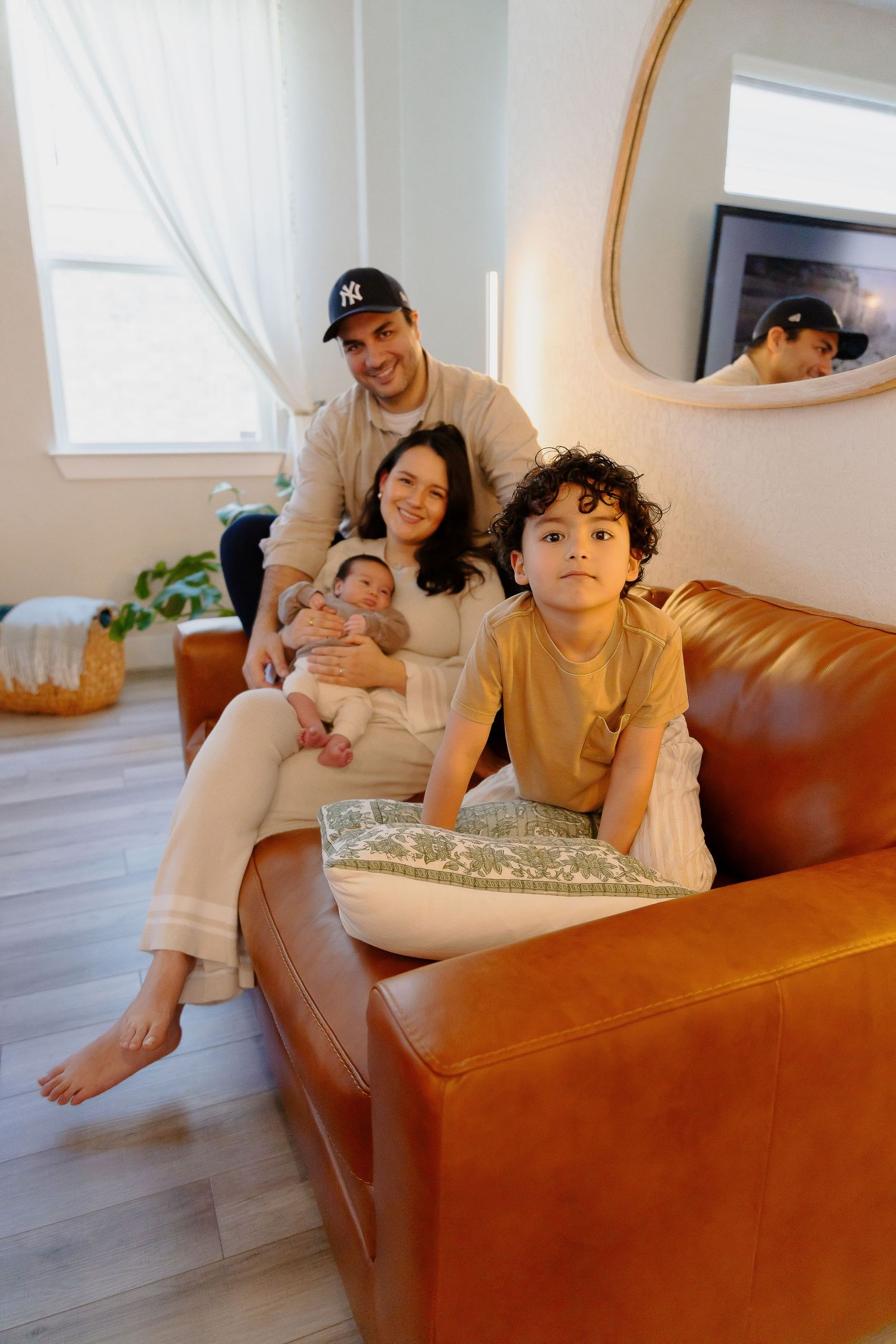 A cozy family scene lounging together on a brown leather couch in a bright living room with minimalist decor.