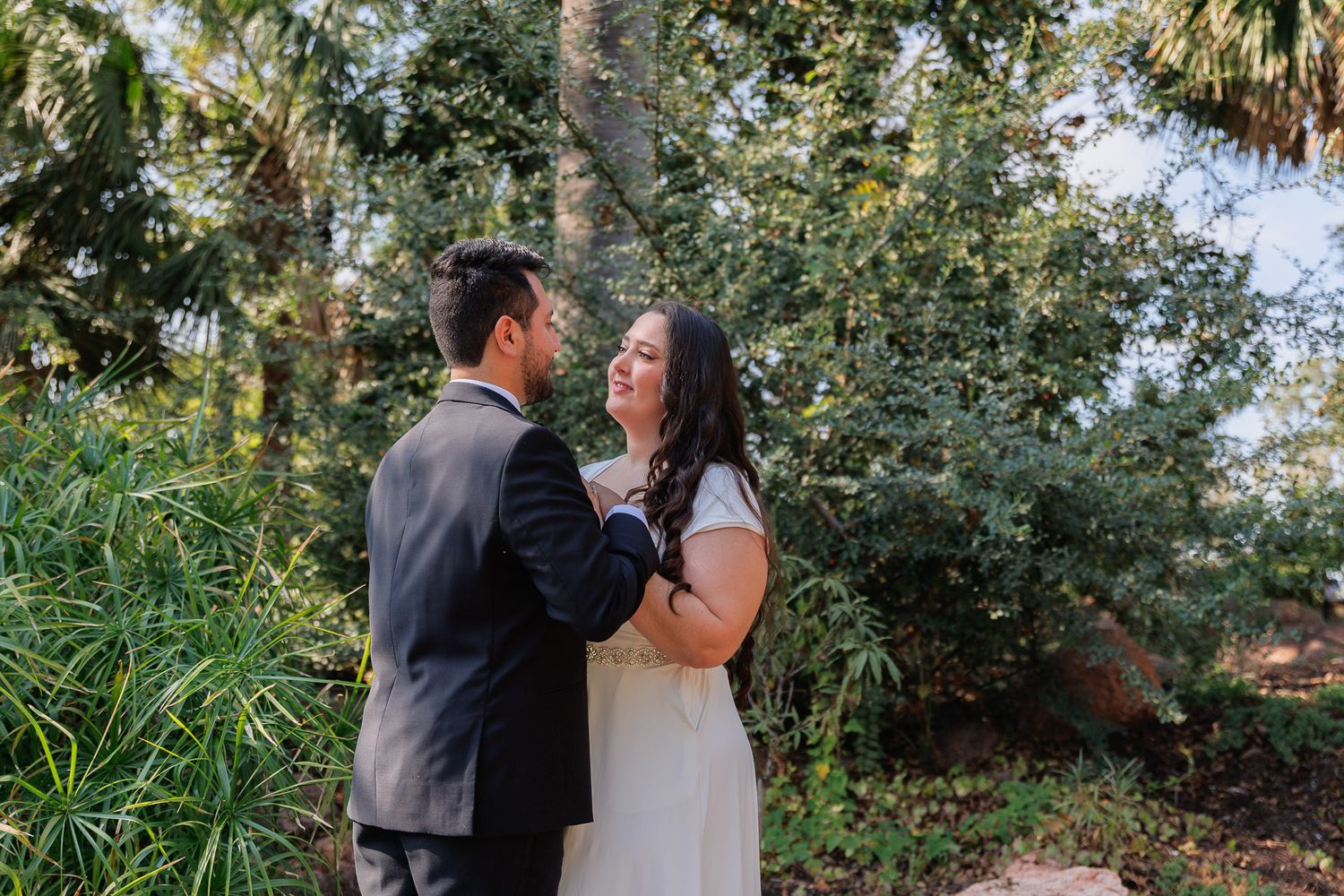 A couple shares a romantic moment in a lush garden setting during their wedding day.