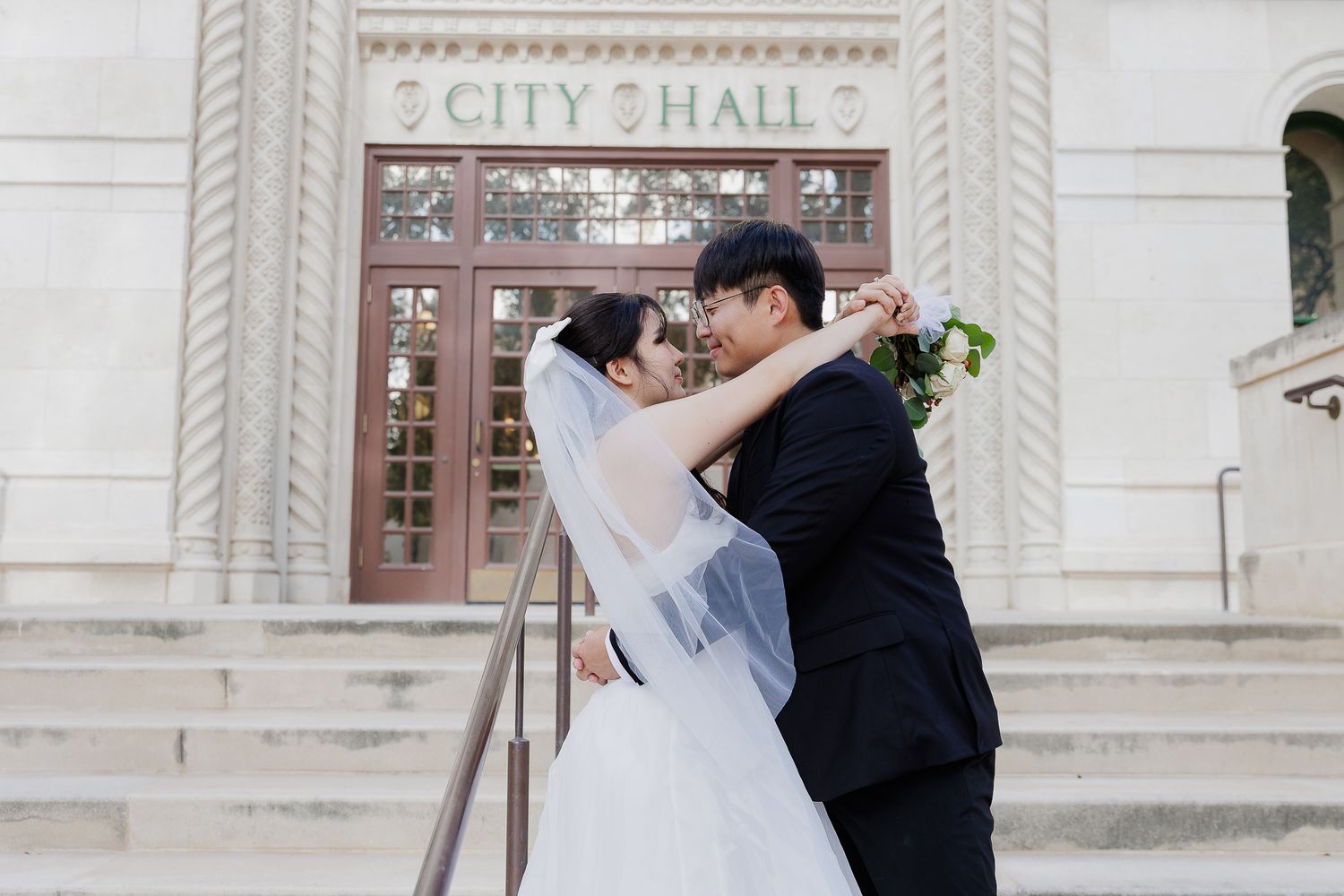 Couple dancing together in front of an ornate city hall building with white stone architecture.