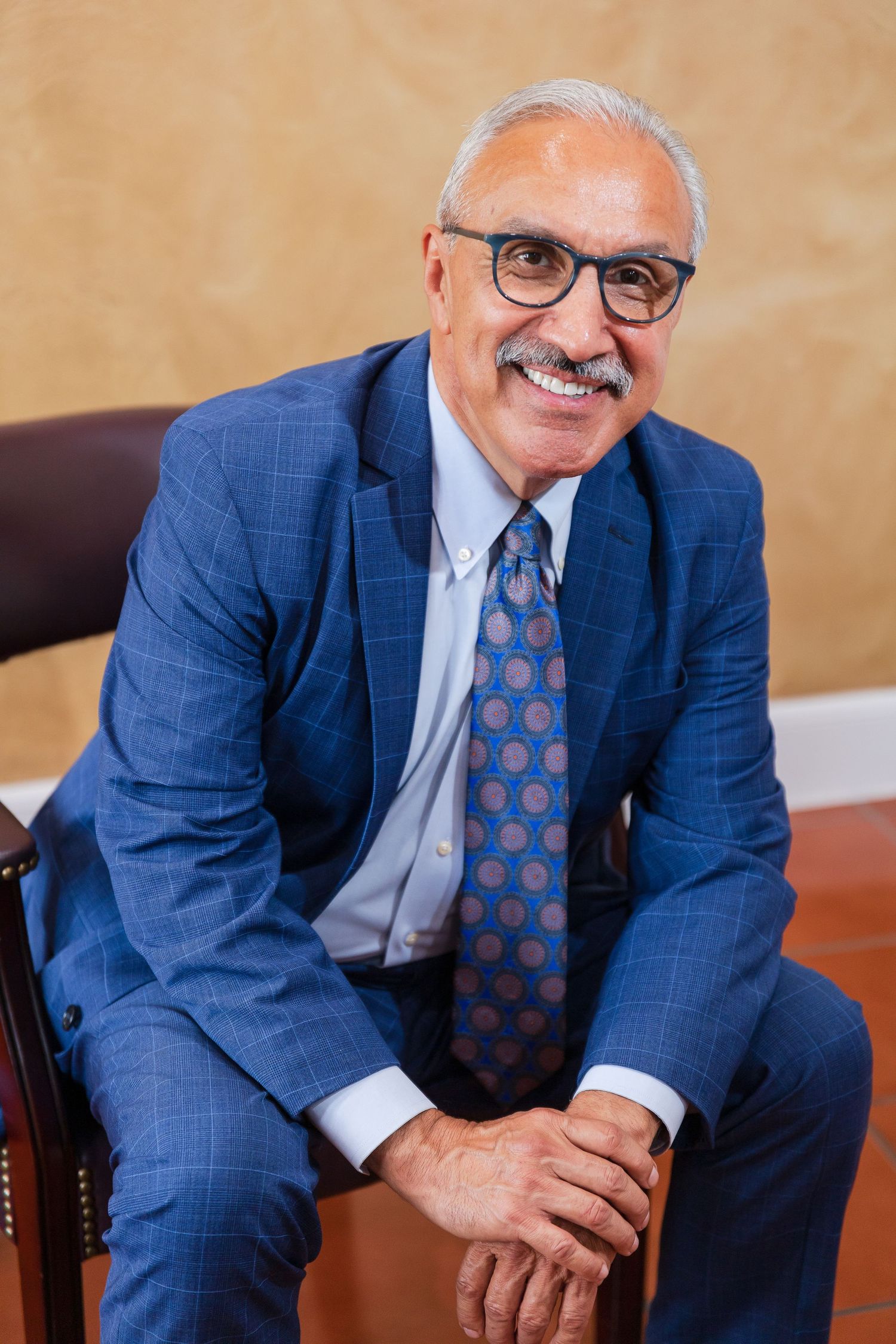 Experienced attorney in blue suit and patterned tie seated in professional office environment.