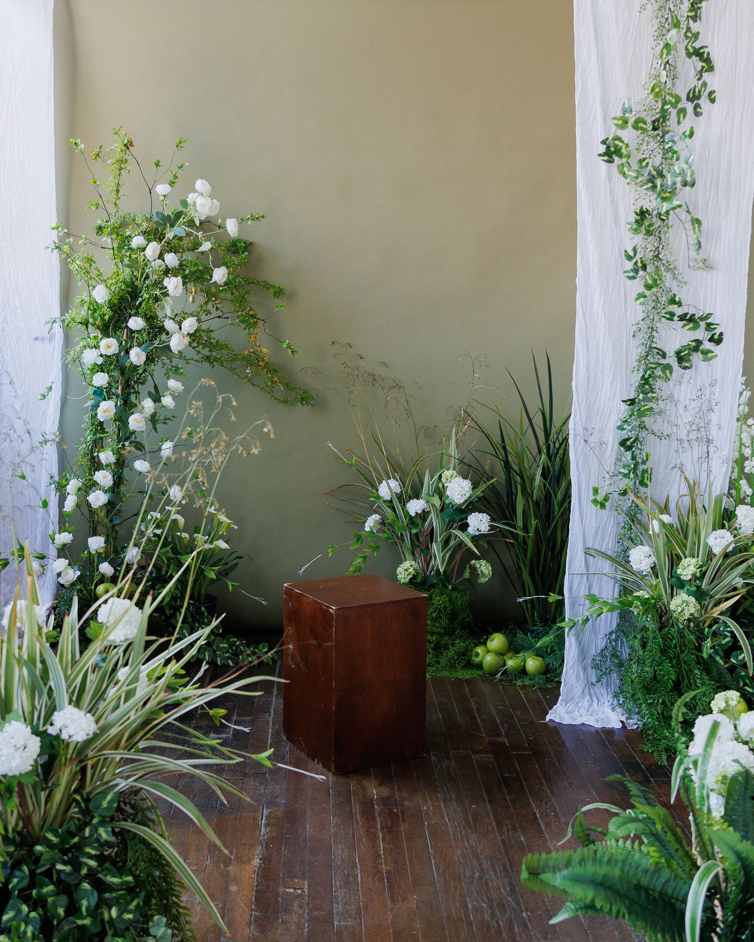 White delphinium flowers and green vines grow along a rustic wooden deck railing in a garden setting.