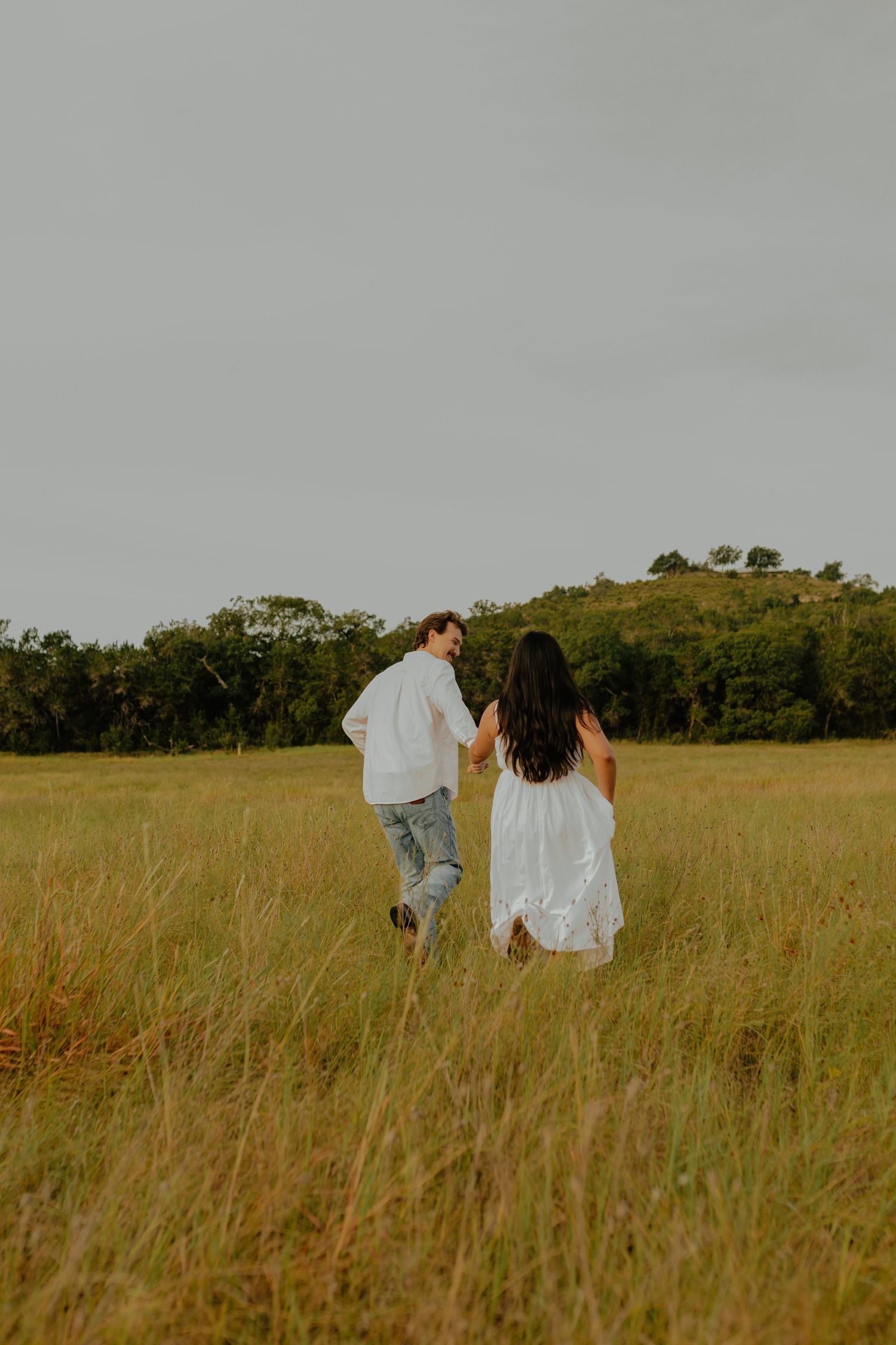 Couple walks through tall golden grass in sunny meadow.