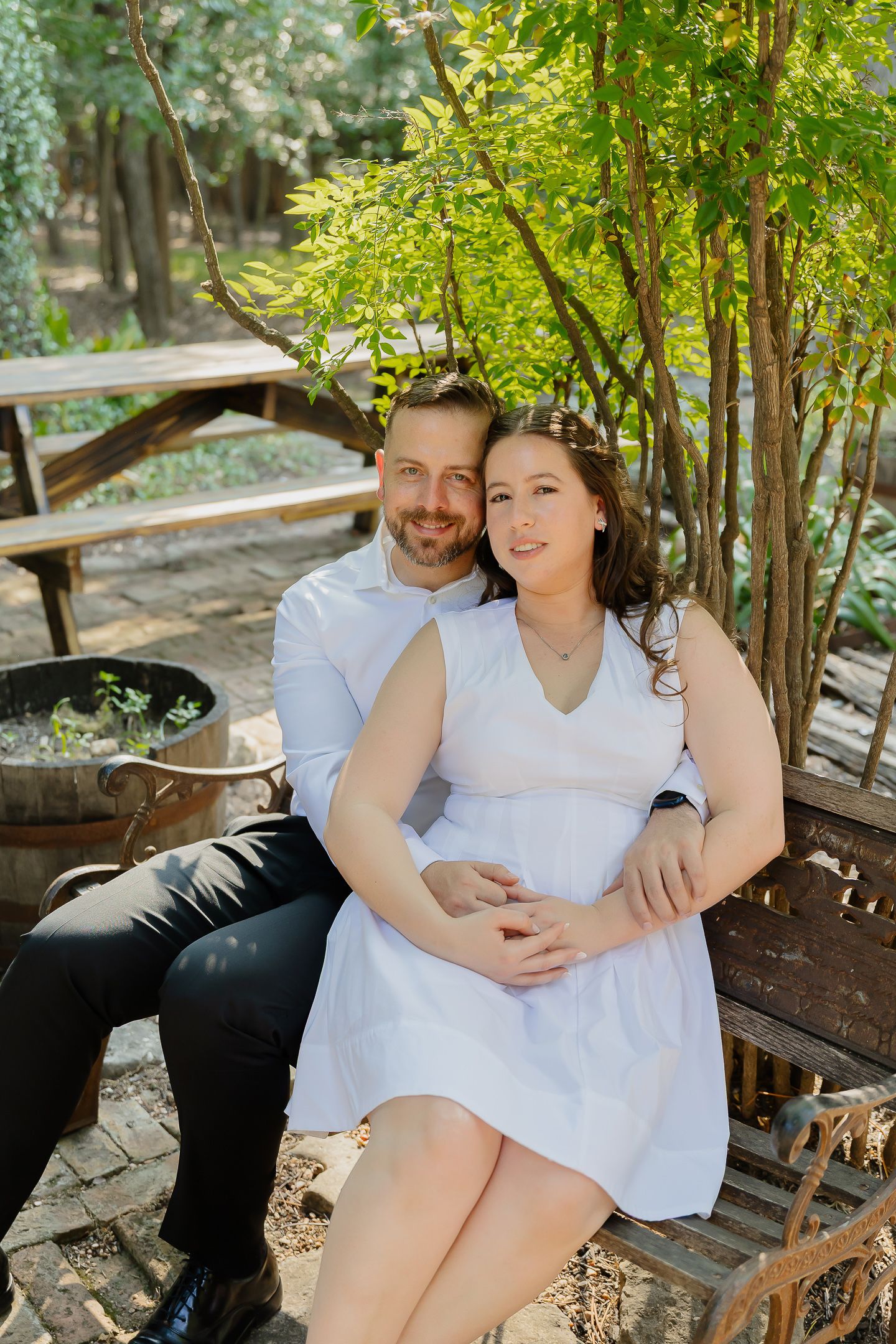 Happy couple relaxes together on a wooden bench surrounded by lush green foliage in a garden setting.
