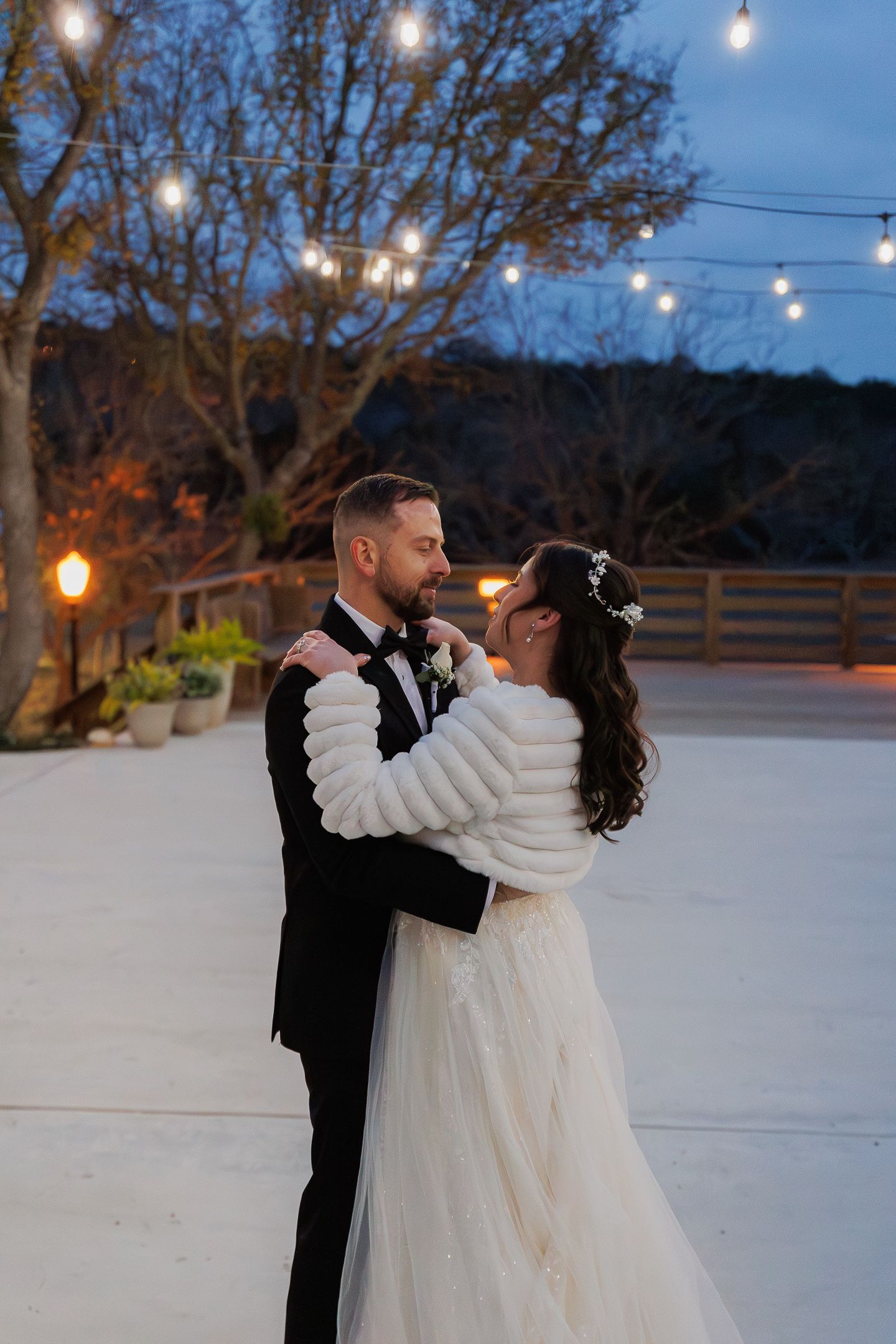 A romantic winter wedding dance sequence captured at dusk with string lights glowing overhead in the snowy outdoor setting.
