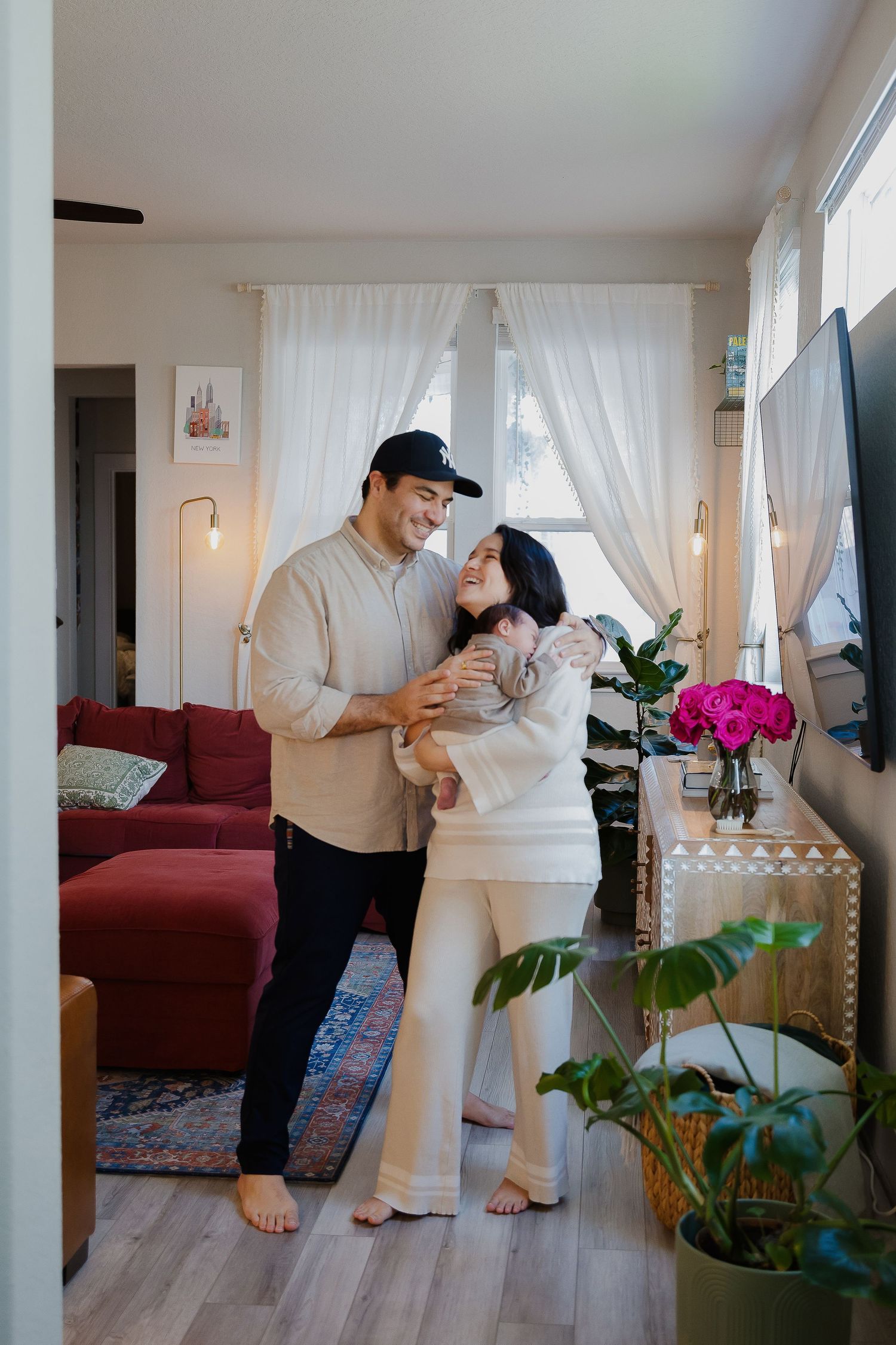 Two people share an intimate moment in a cozy living room with white curtains, red sofa and houseplants.