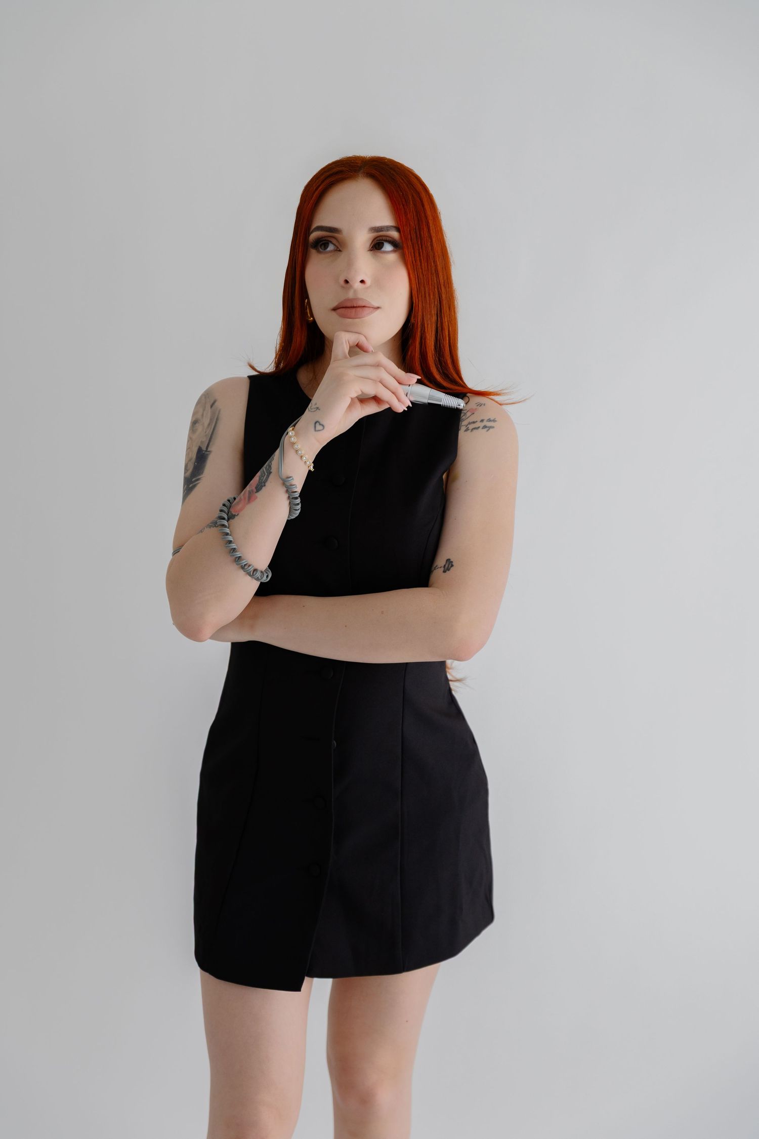 Redheaded woman in black dress strikes thoughtful pose against white backdrop.