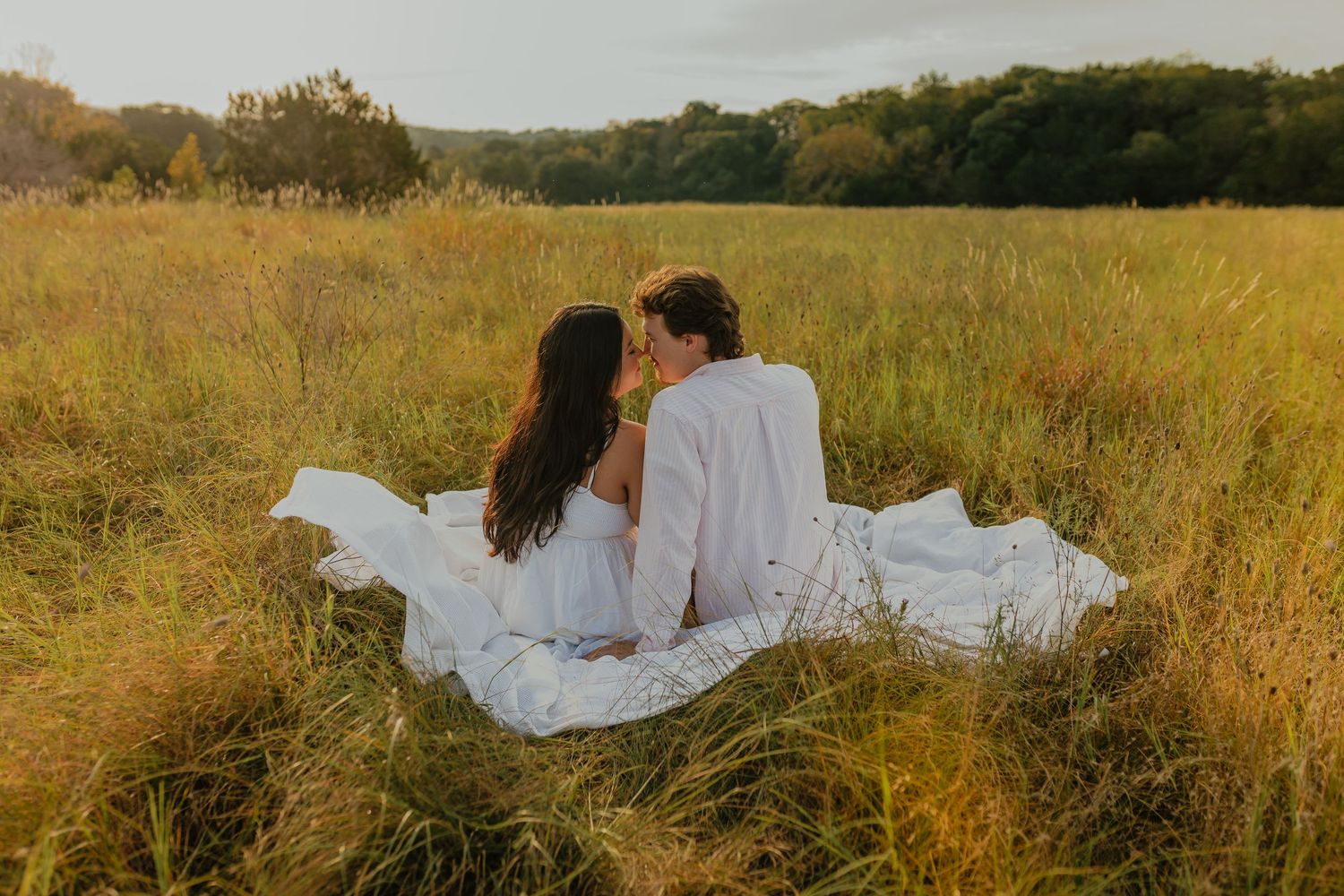 Couple enjoys peaceful moment on white blanket in golden autumn field.