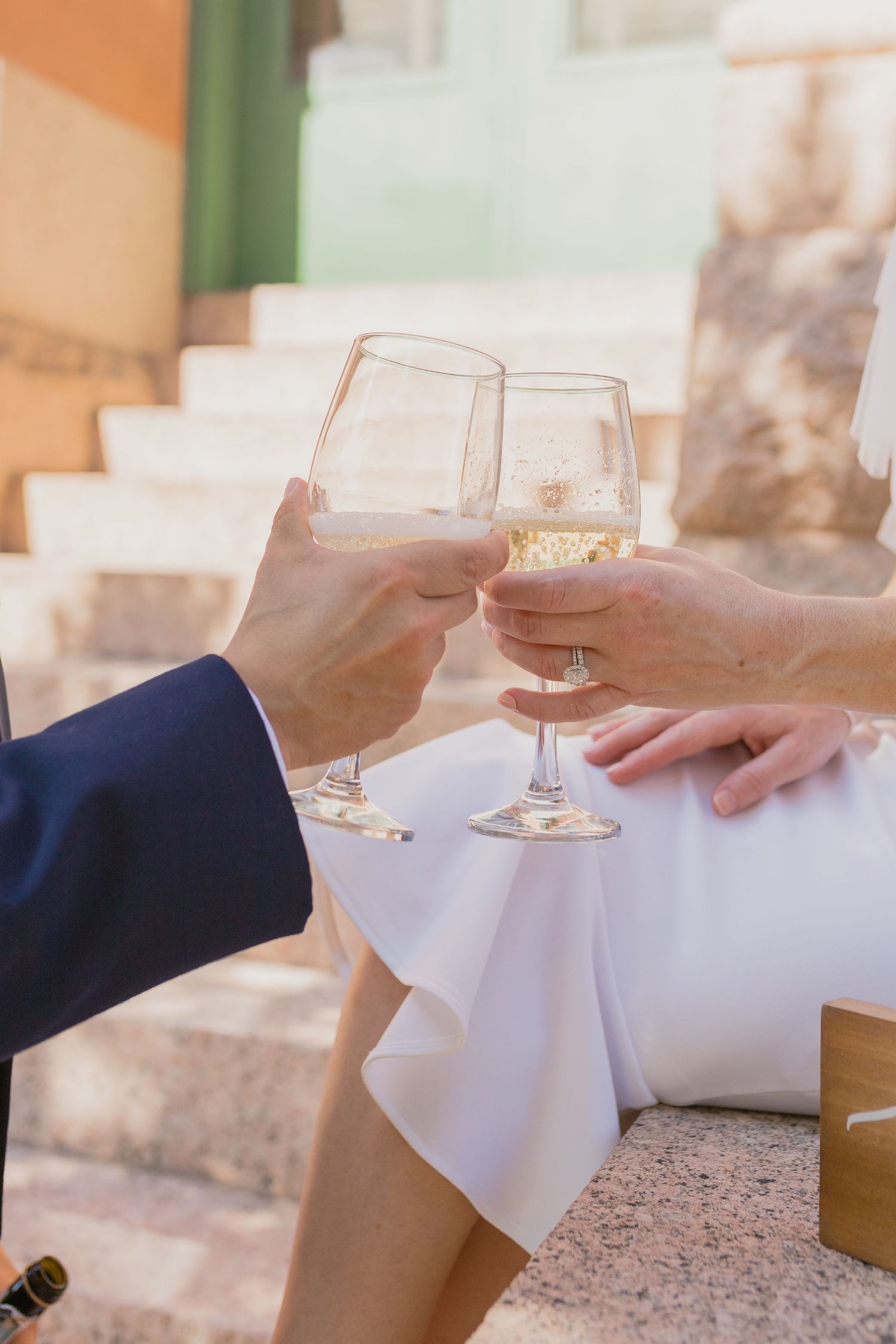 Two hands toast with wine glasses against a white tablecloth background.