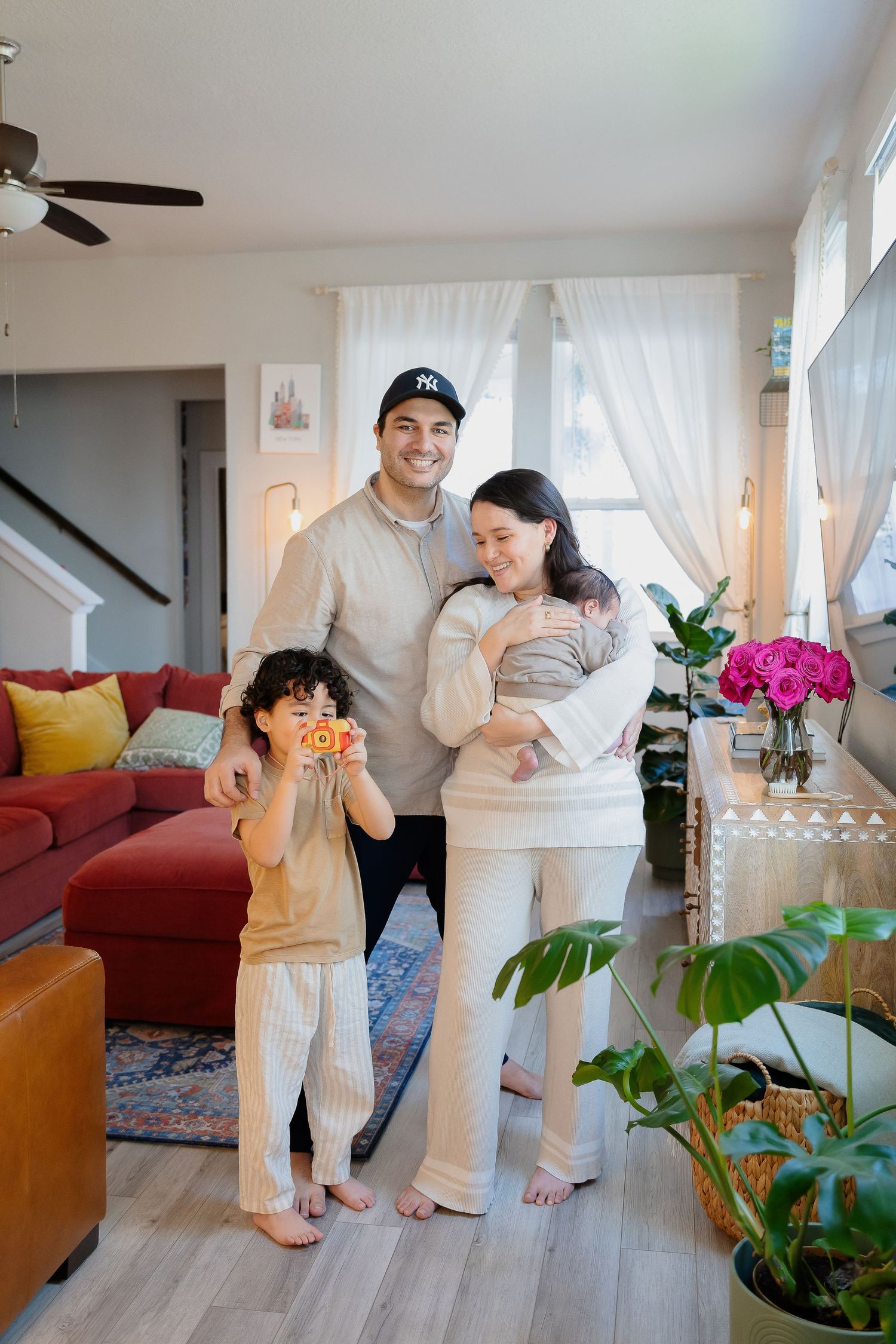 Family in casual wear poses together in their cozy living room with colorful decor and plants.