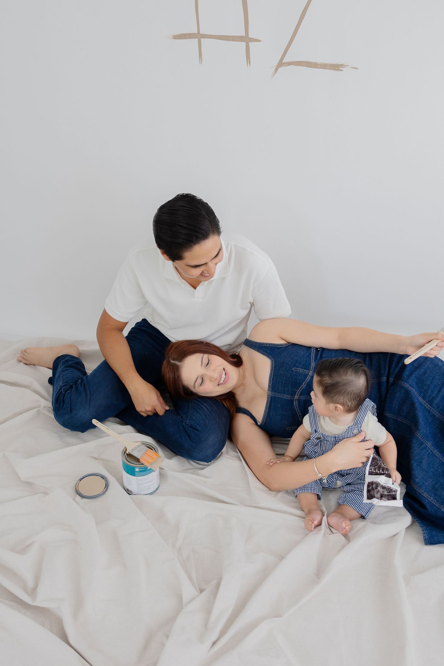 A family relaxes together on white bedding while looking at ultrasound photos.
