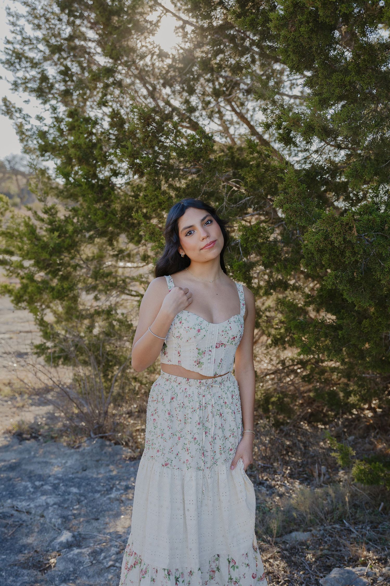 Woman in a floral dress poses against a desert landscape with juniper trees.