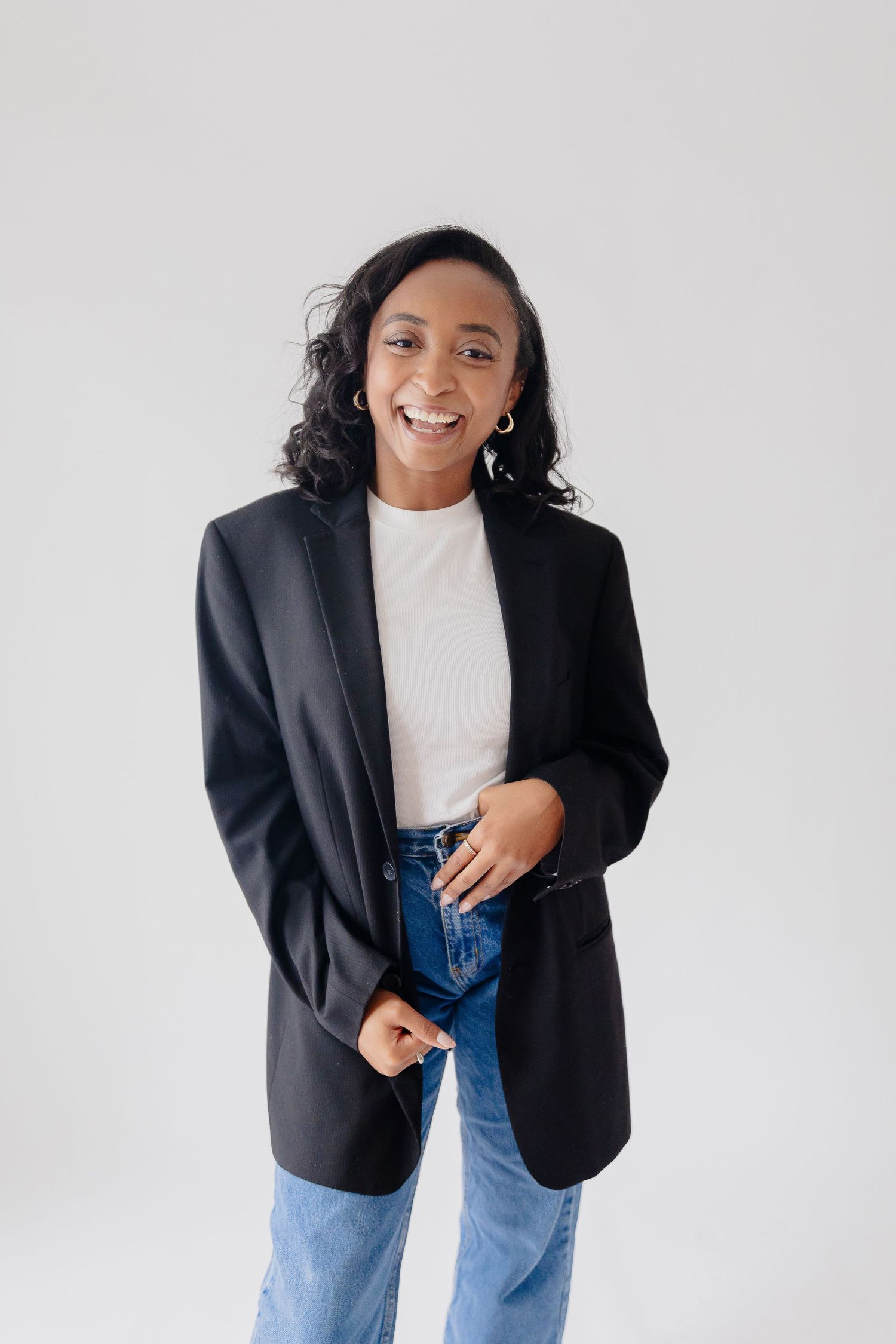 Casual portrait of a person wearing a black blazer and jeans against a white background.