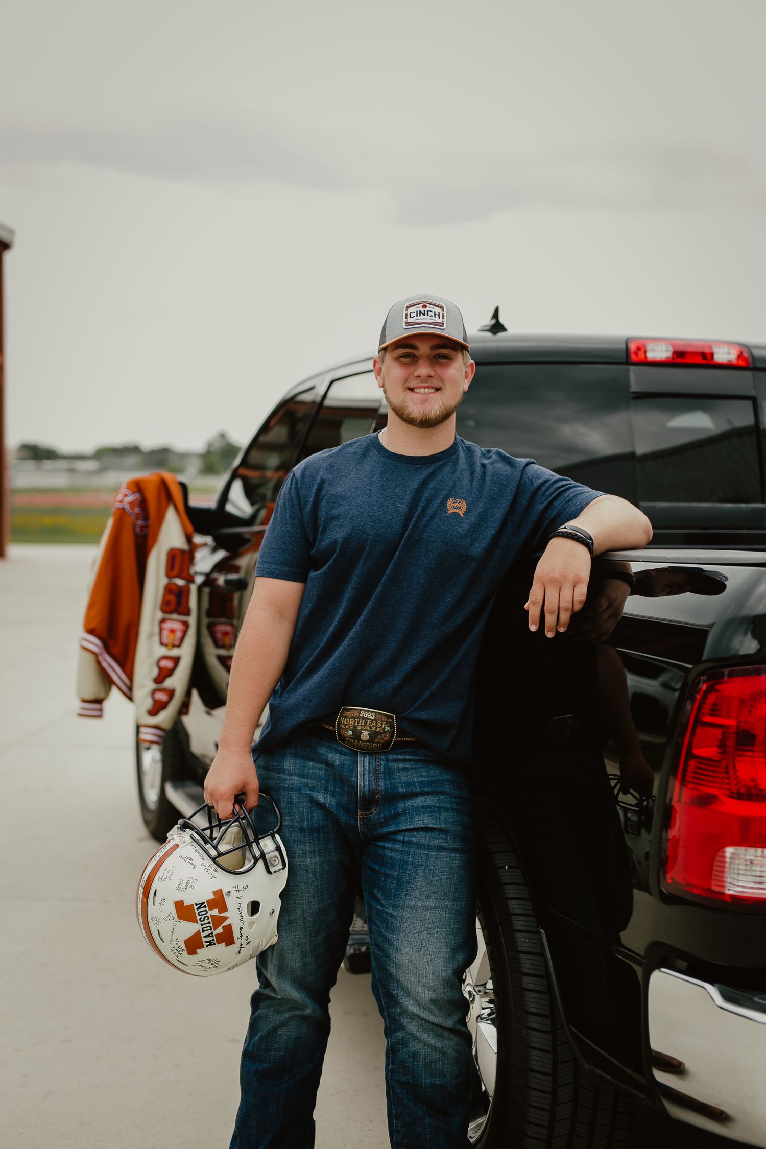 Student athlete poses with football helmet next to pickup truck in parking lot.