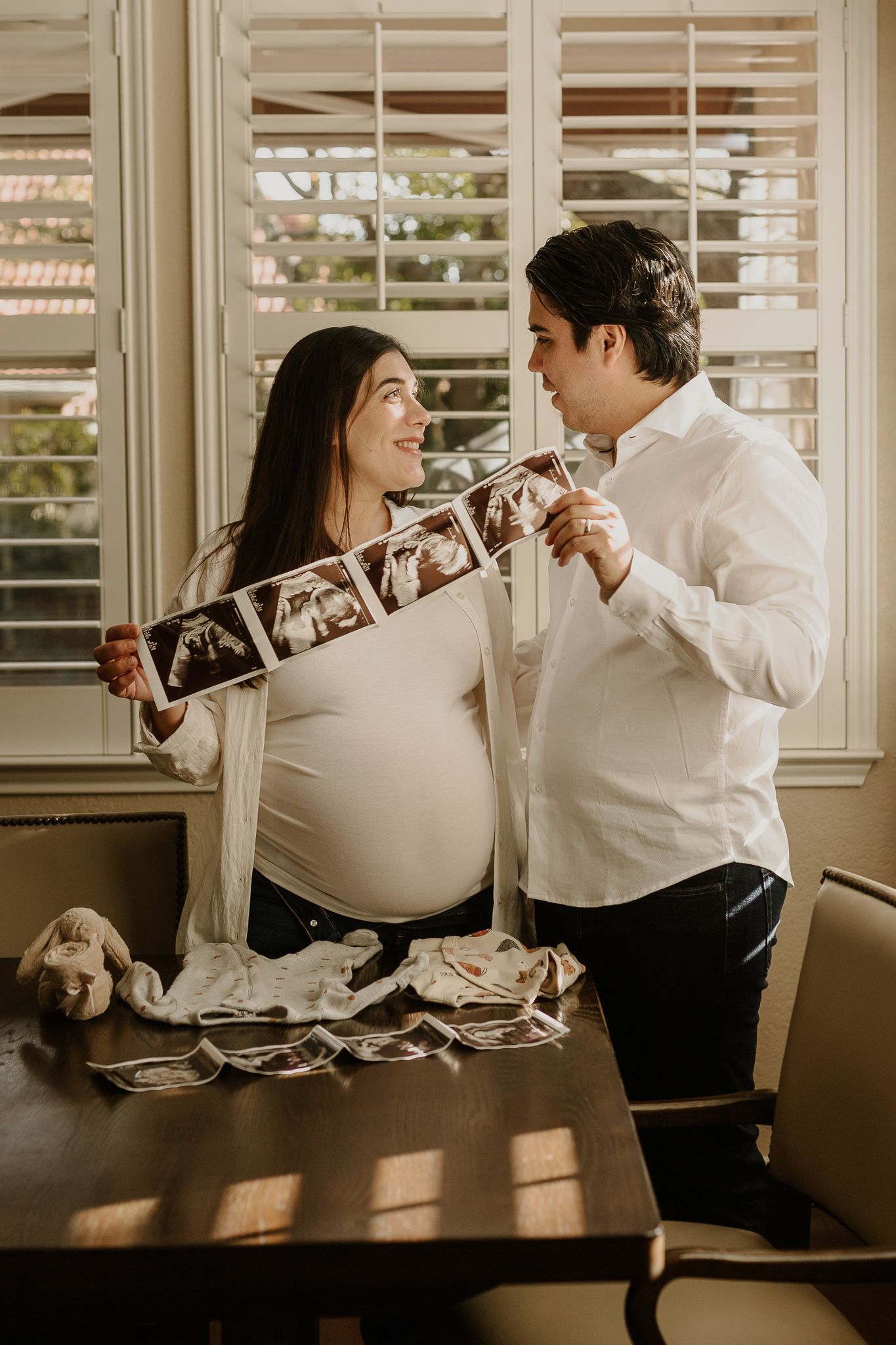 Expecting parents share joyful moment while holding ultrasound strip in dining room.