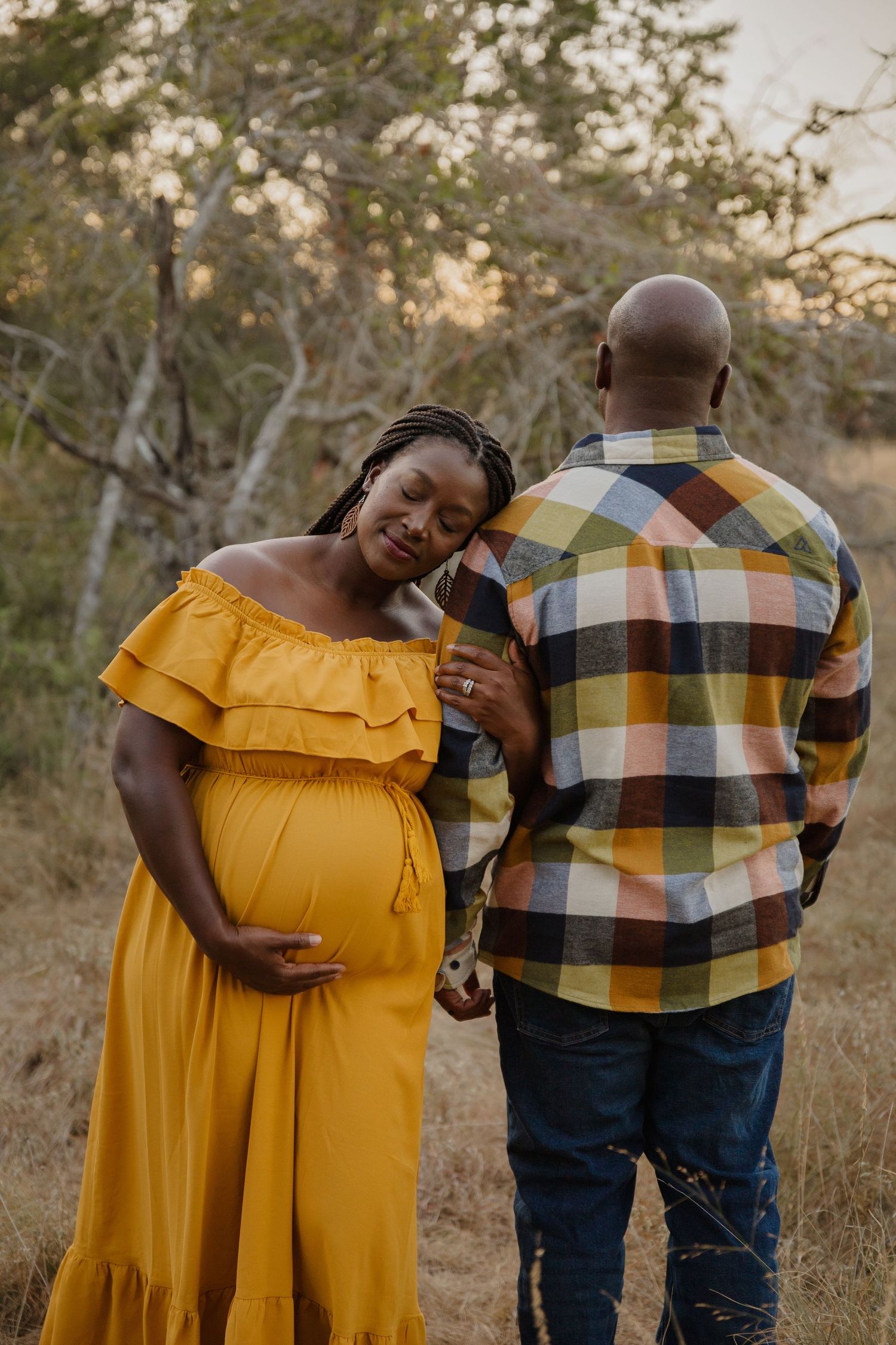 Expectant couple shares tender moment in outdoor setting at sunset.