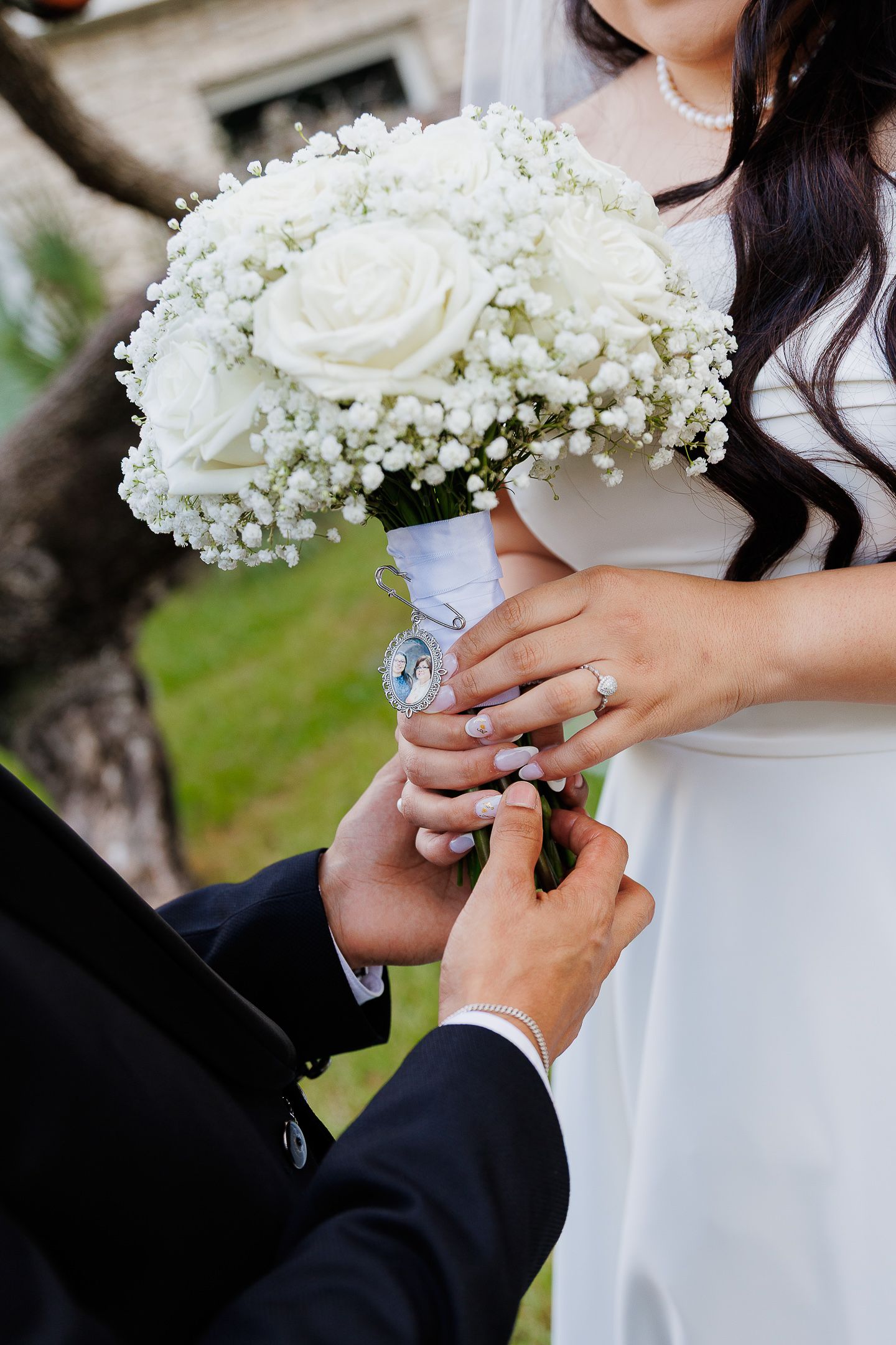 Close-up of couple's hands holding delicate white rose and baby's breath wedding bouquet during outdoor ceremony.