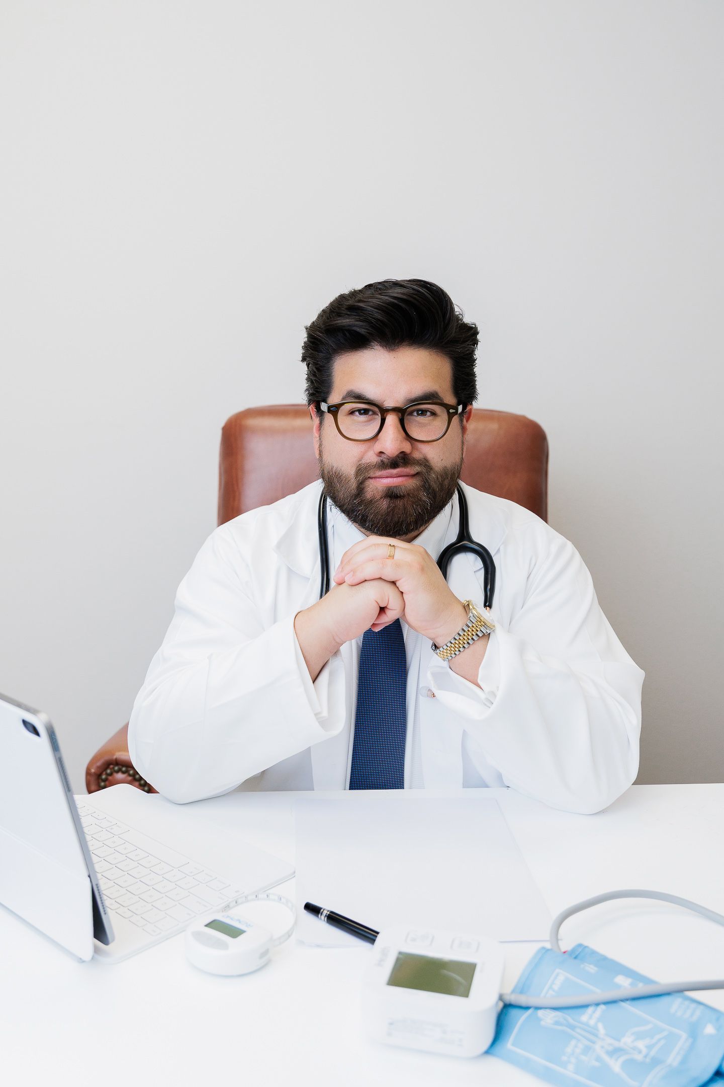 Medical professional in white coat and tie reviews digital health information at desk with tablet display.