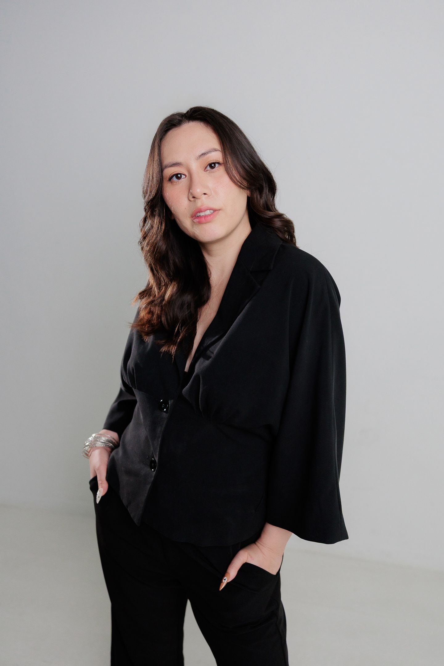 Woman in black oversized blazer and pants poses confidently against a light gray background.