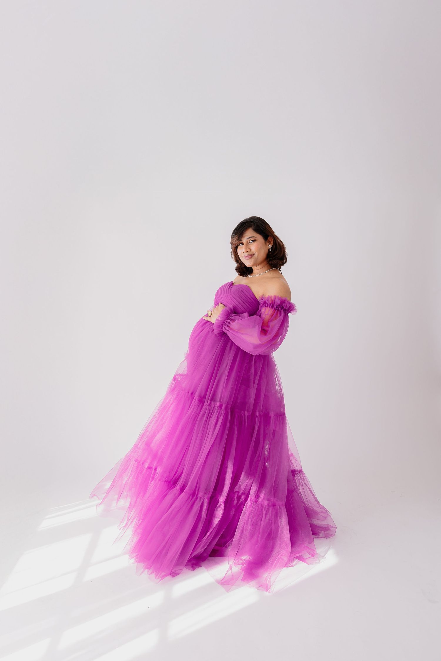 An expectant mother twirls in a dramatic purple tulle gown against a white backdrop.