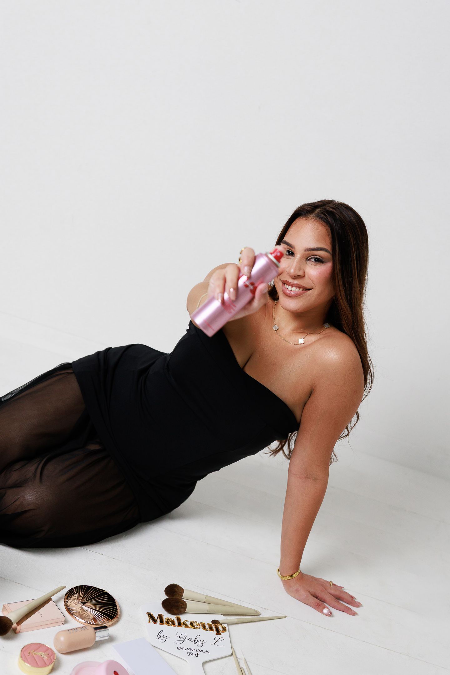 A person in a black dress poses on a white studio floor with books and papers scattered around them.