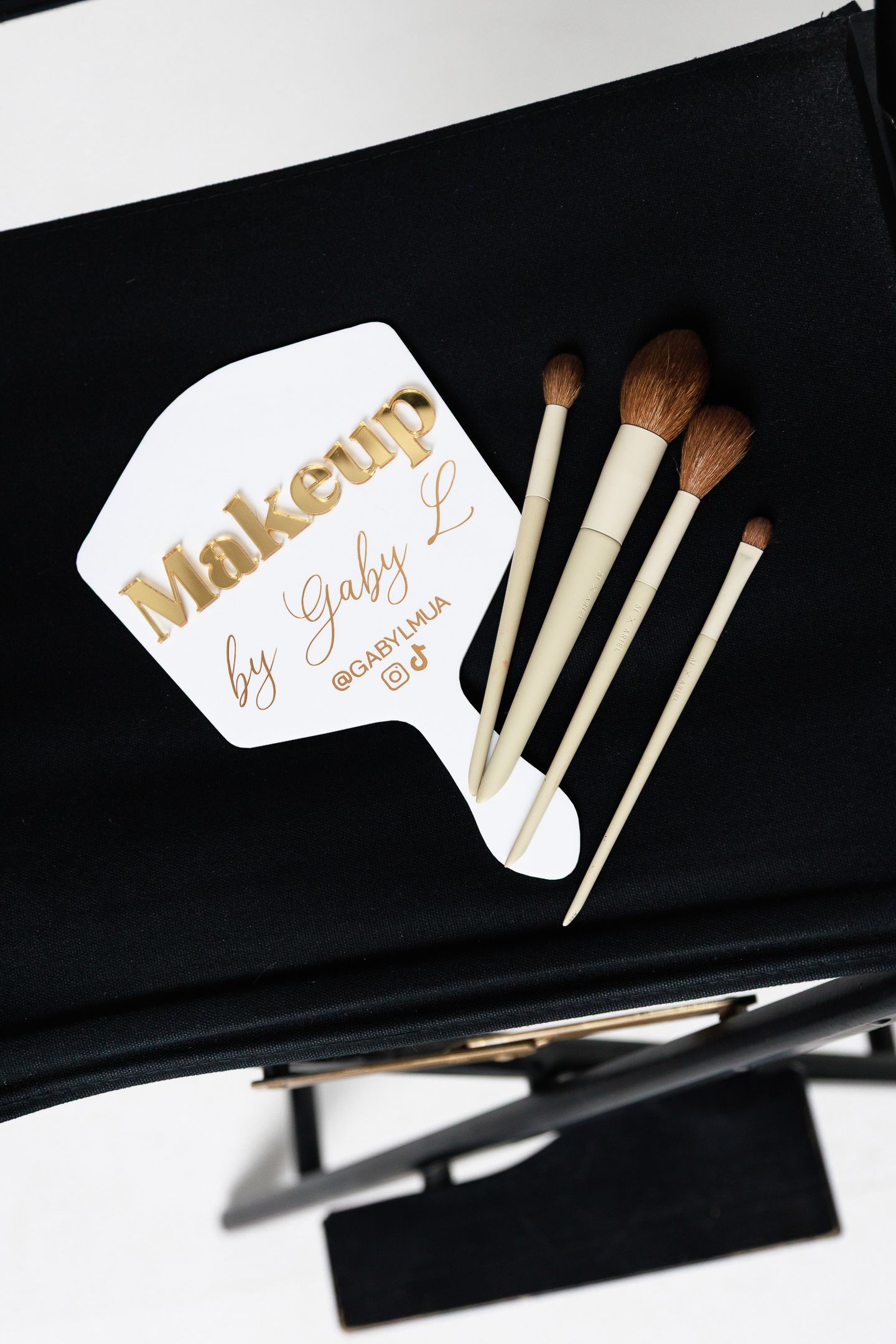 Makeup brushes arranged with white and gold lettering cards on black background in artistic composition.