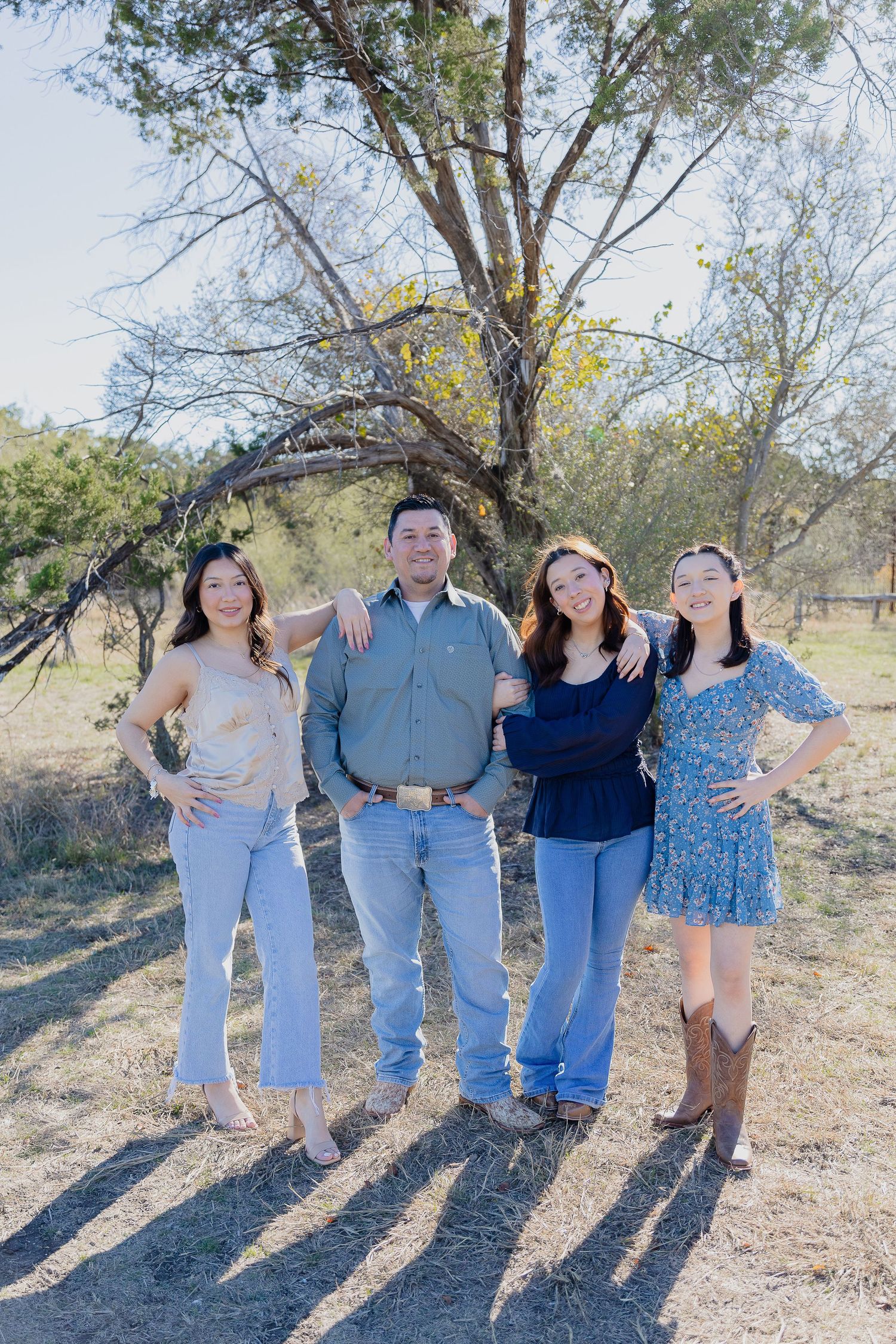 Four people stand together outdoors on a sunny day with trees and natural scenery in the background.
