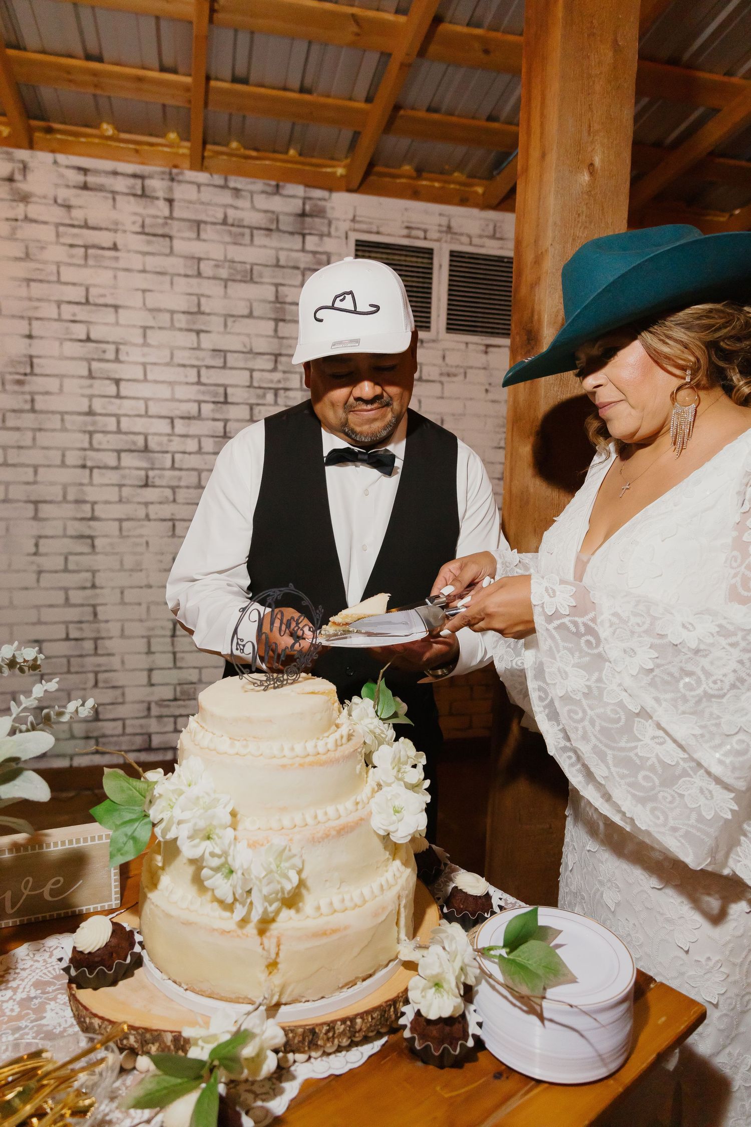 Wedding couple cuts elegant white tiered cake decorated with flowers at reception.