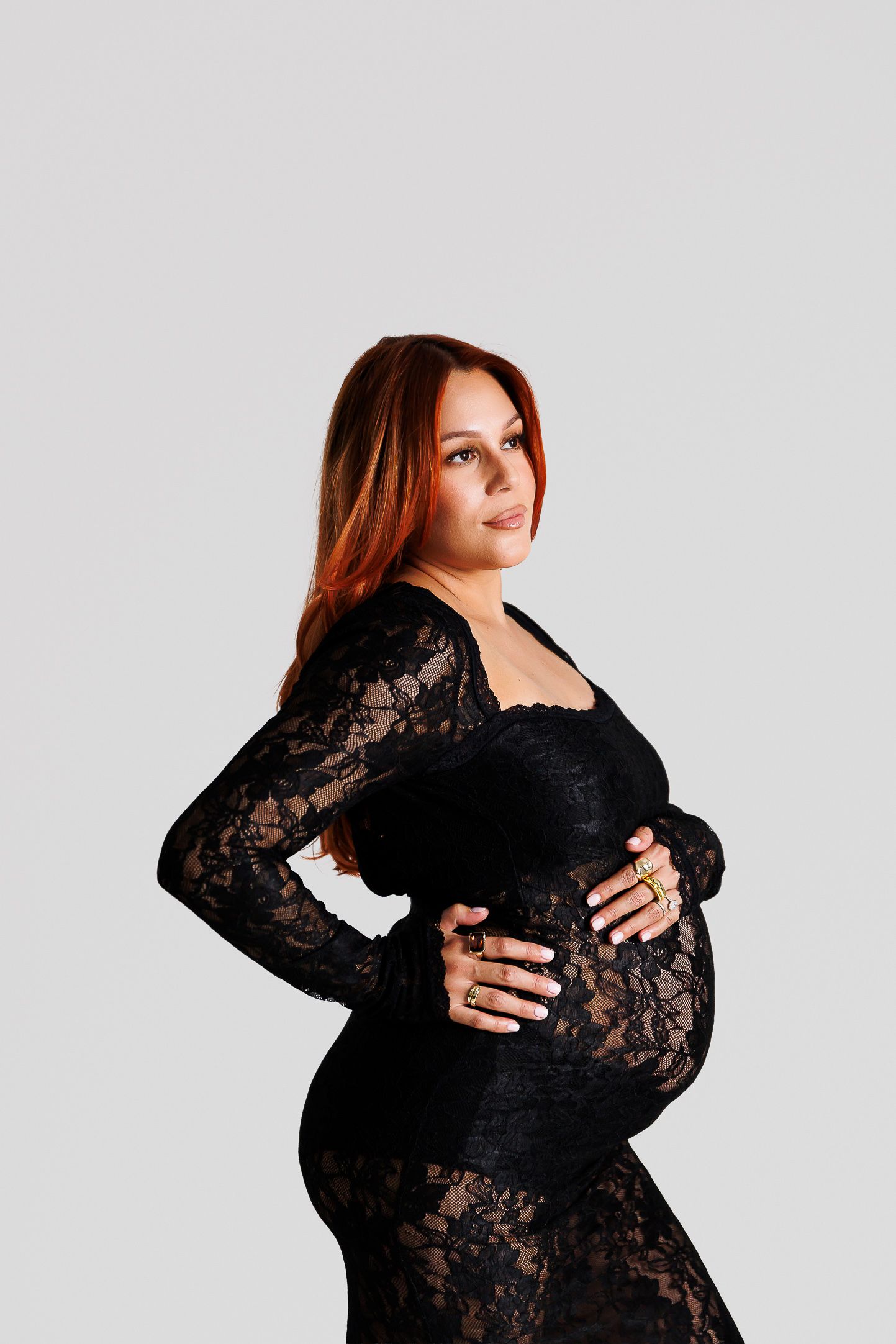 A figure in a black lace maternity dress poses in a series of artistic pregnancy portraits against a light background.