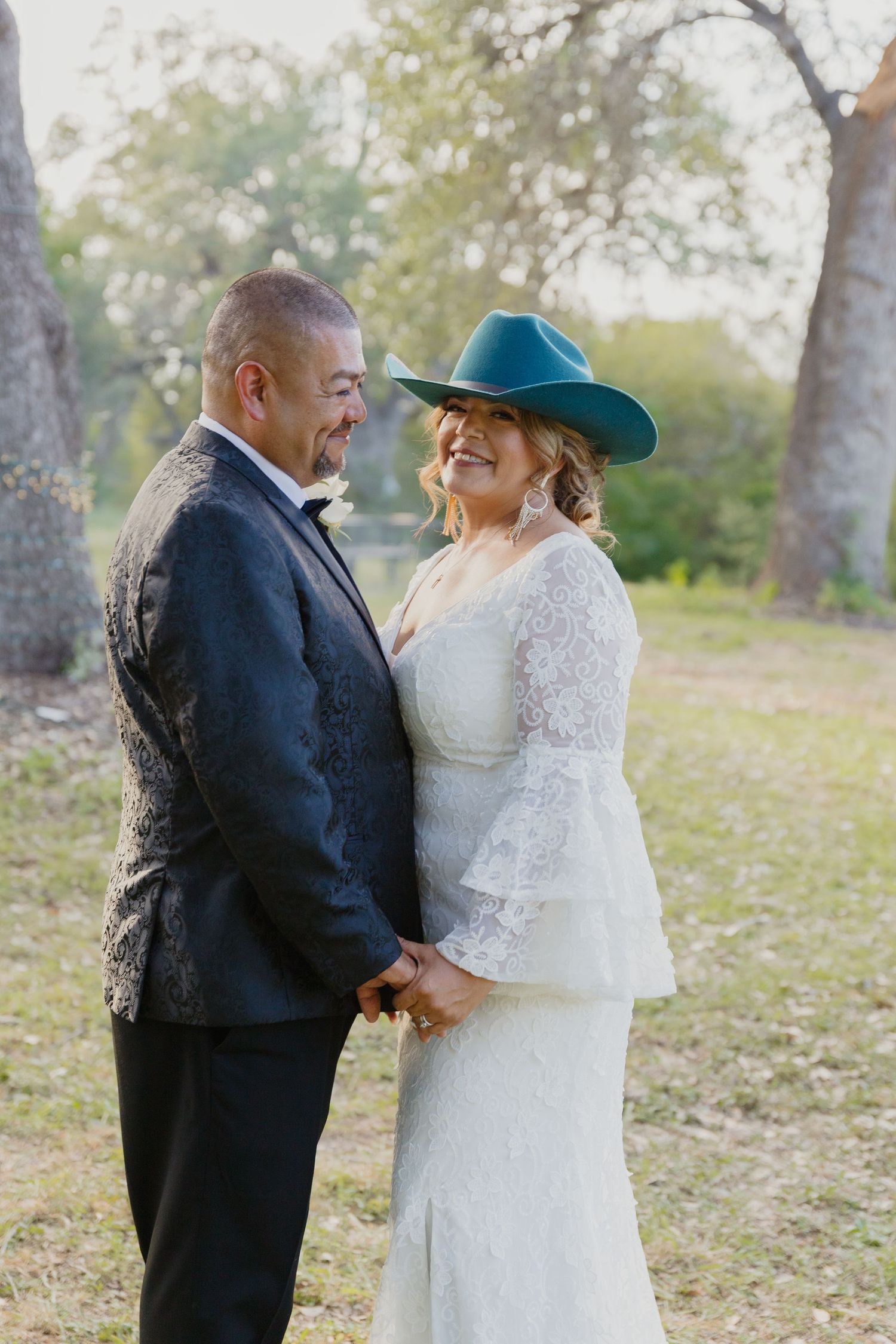 Couple in western wedding attire share intimate moment outdoors at sunset.