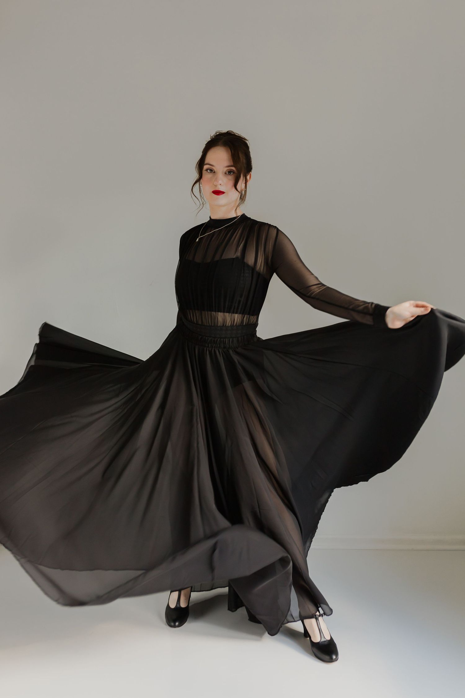 Elegant model in black sheer gown poses gracefully showing dress movement.