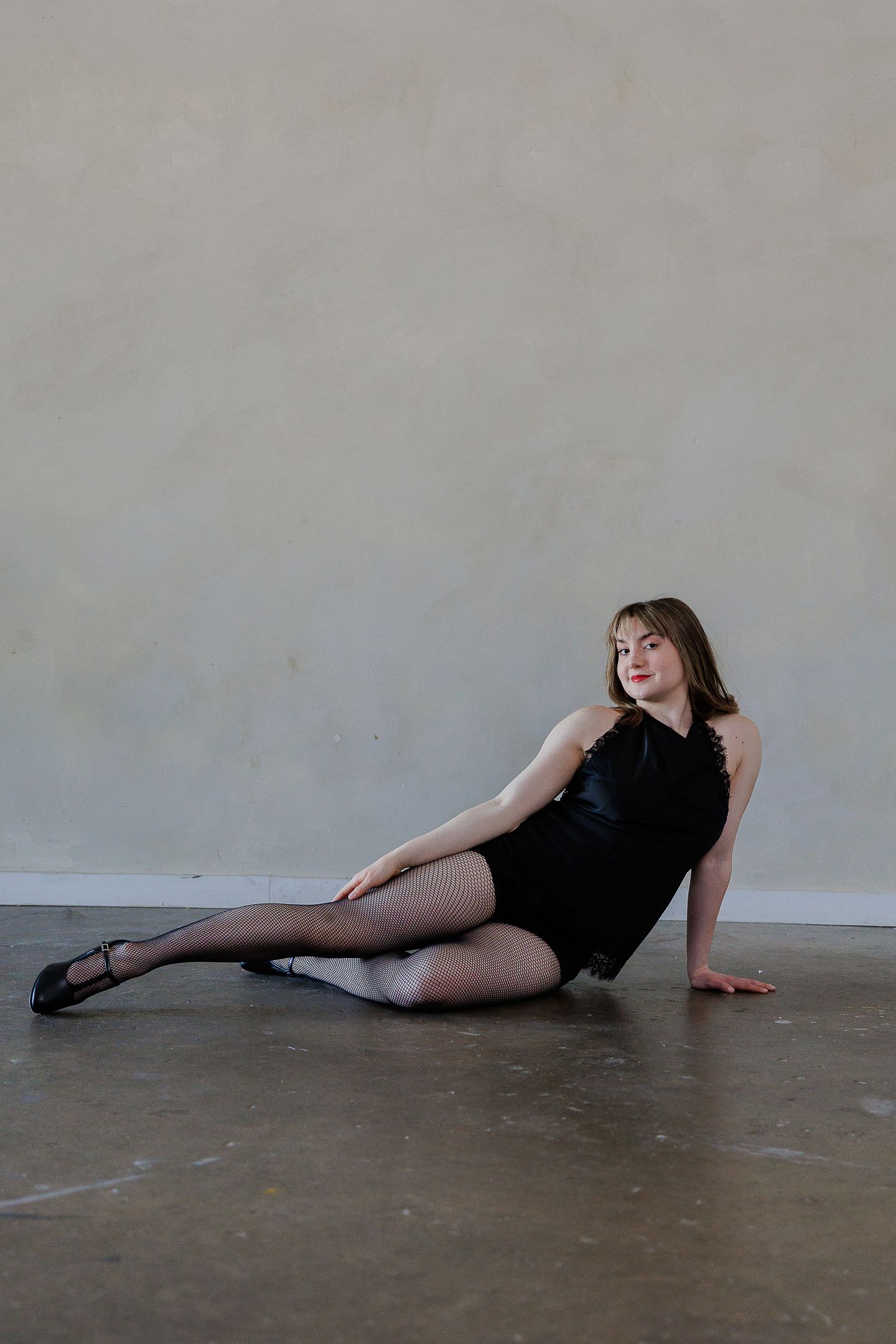 A dancer in black attire performs a graceful reclining pose sequence on a concrete floor.