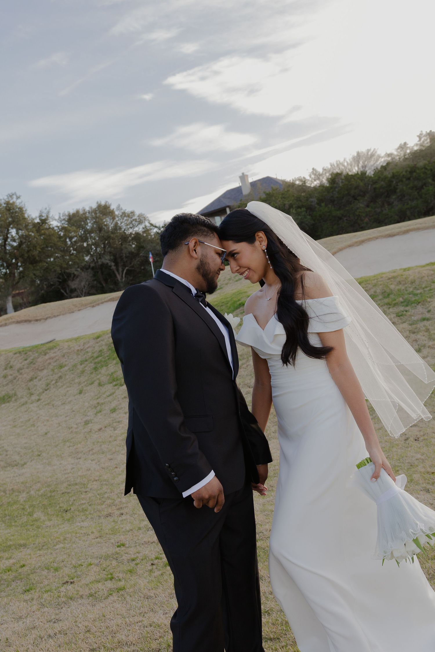 A romantic moment between newlyweds sharing an intimate pose outdoors with a flowing veil.