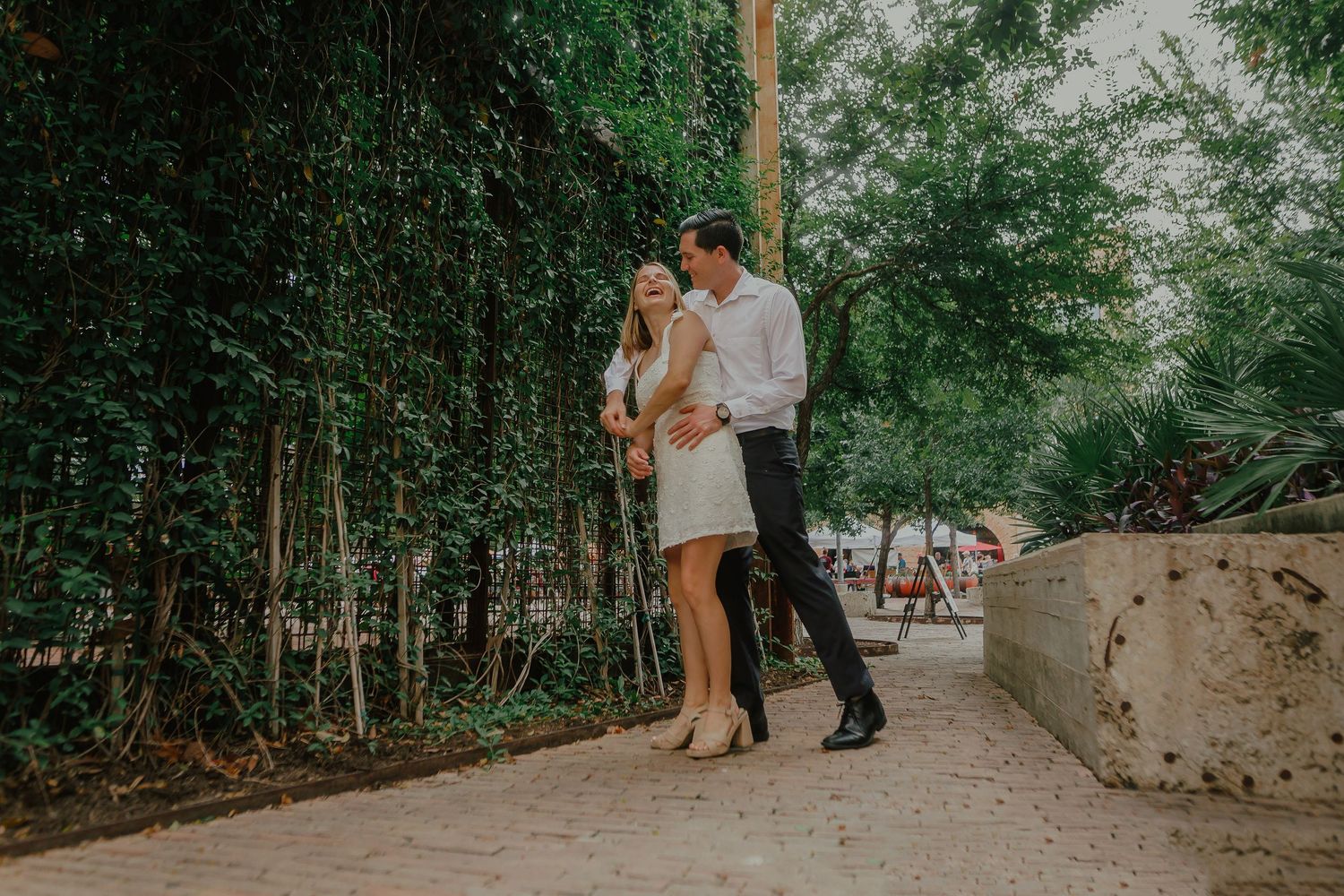 Couple dancing together on a stone path surrounded by lush greenery.