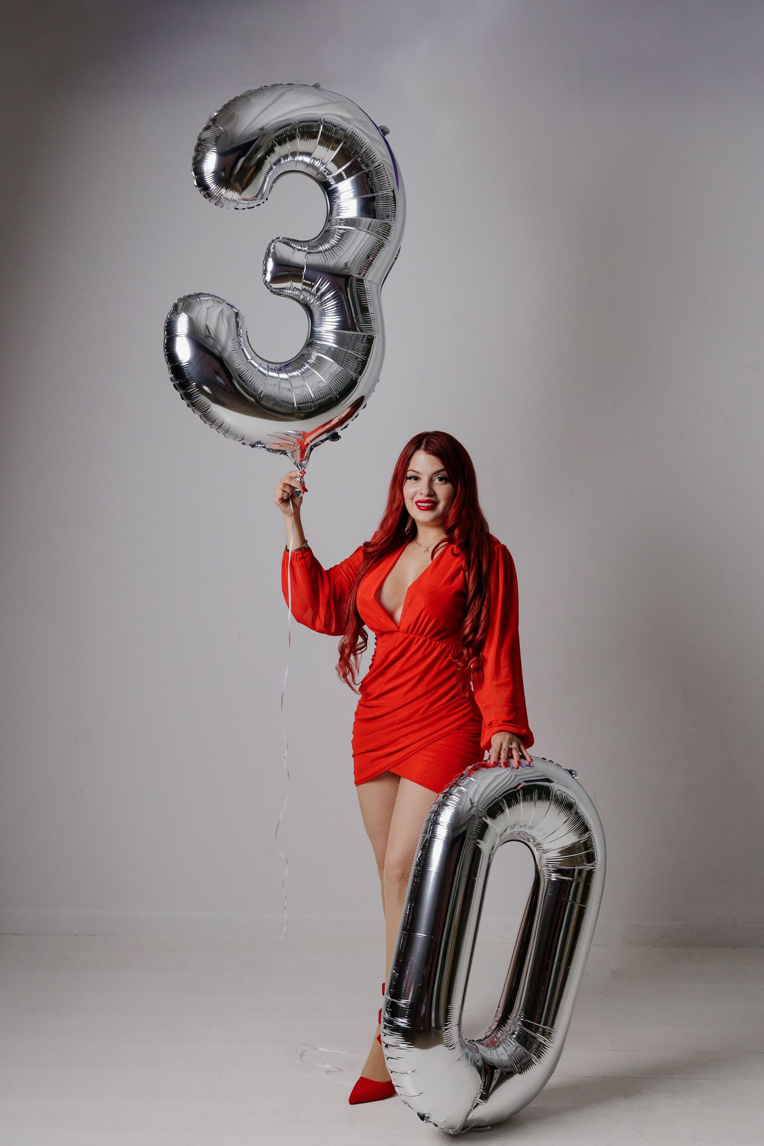 A sequence of photos showing a person in a red dress posing with silver number balloons against a gray backdrop.