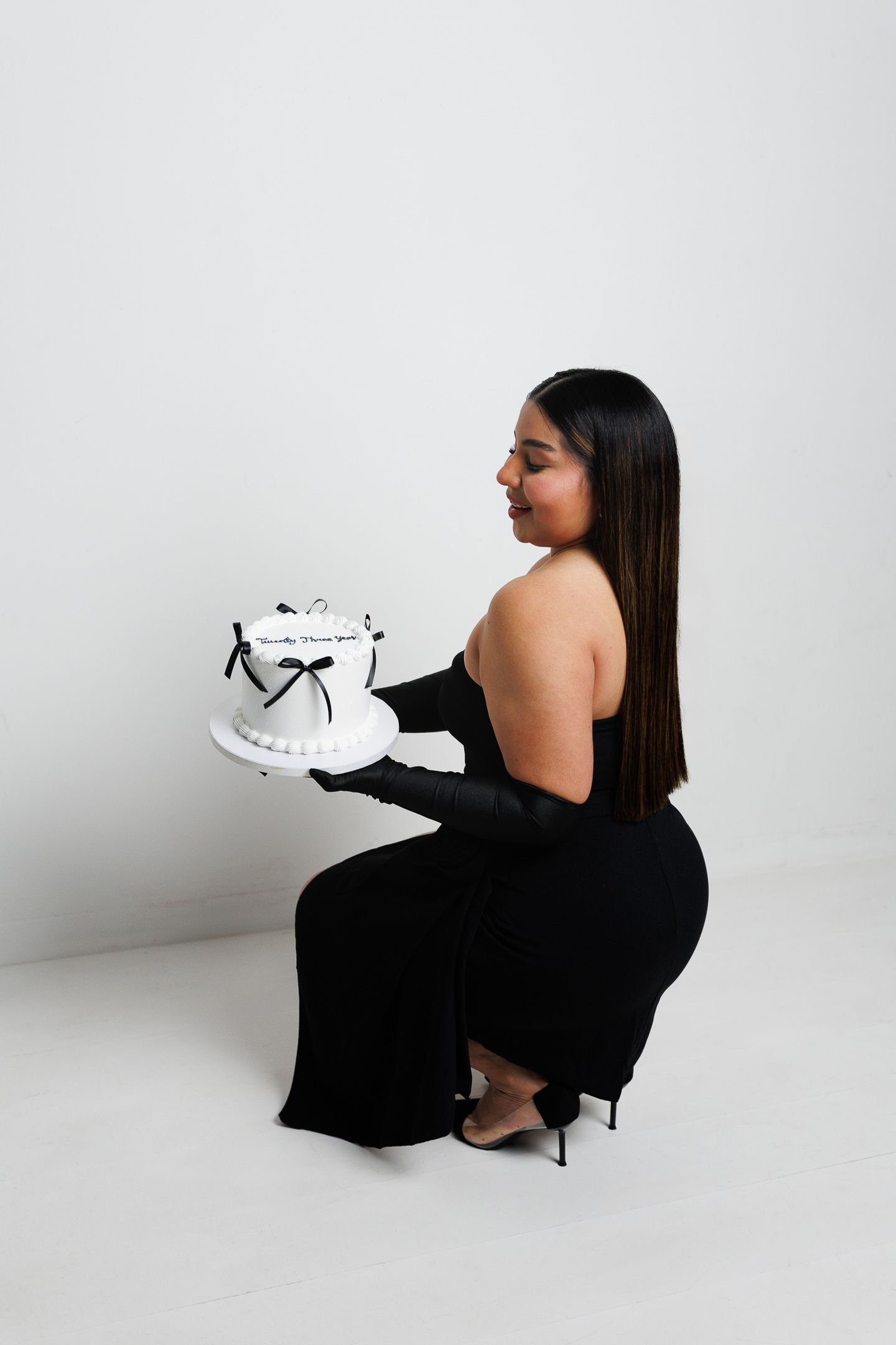 A minimalist fashion shoot featuring a model in a black dress posing with white sneakers against a white backdrop.