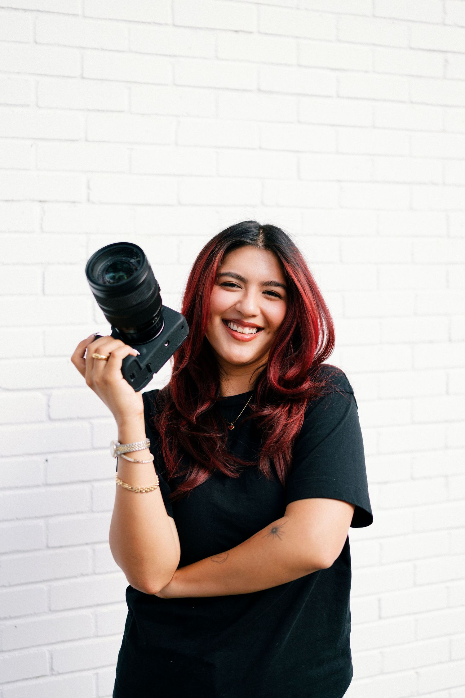 Photographer in black shirt holding camera poses expressively against white wall in three similar shots.