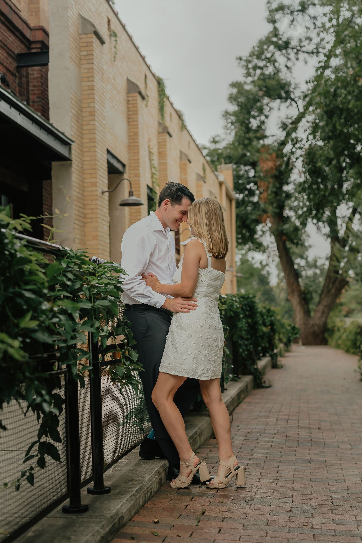 Couple in elegant attire sharing an intimate moment along a brick sidewalk.