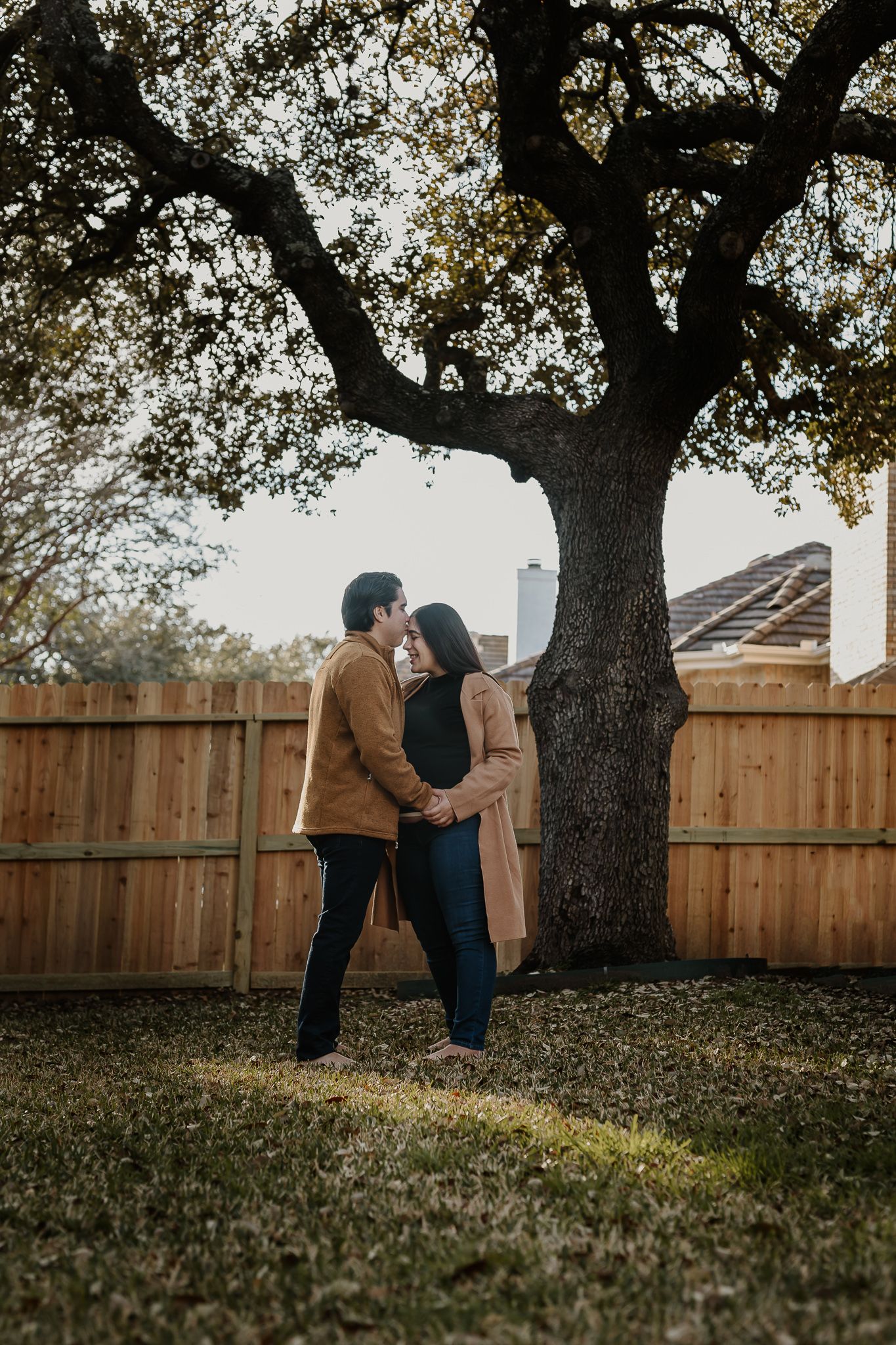 Maternity portrait under large oak tree in backyard during golden hour.