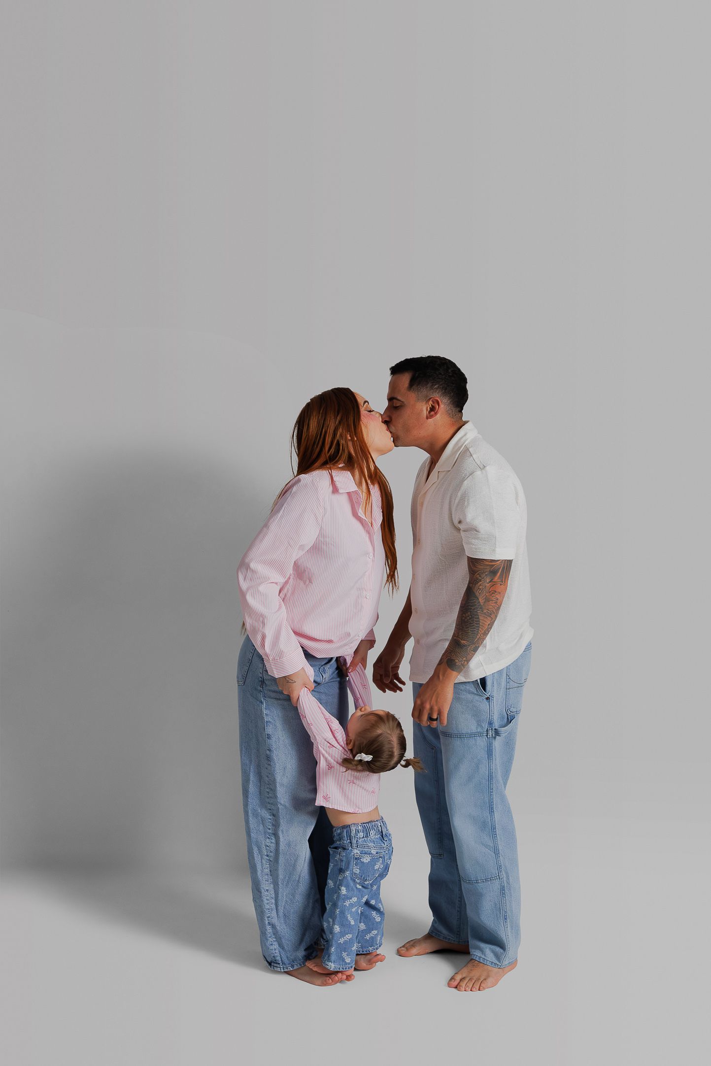A couple in matching blue jeans and casual tops share intimate moments against a gray studio backdrop.