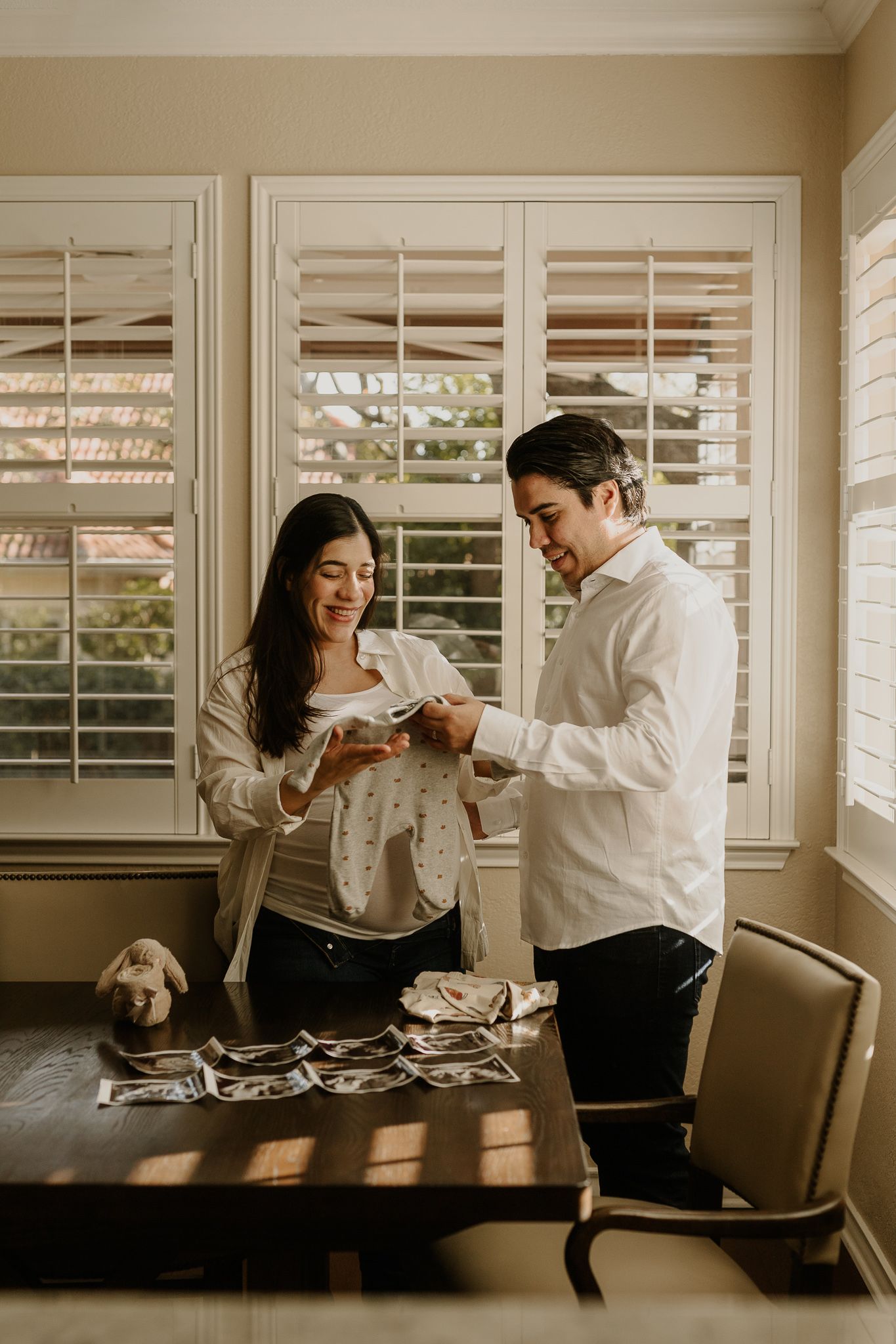 Expectant couple looking at ultrasound photos together in sunlit room with plantation shutters.