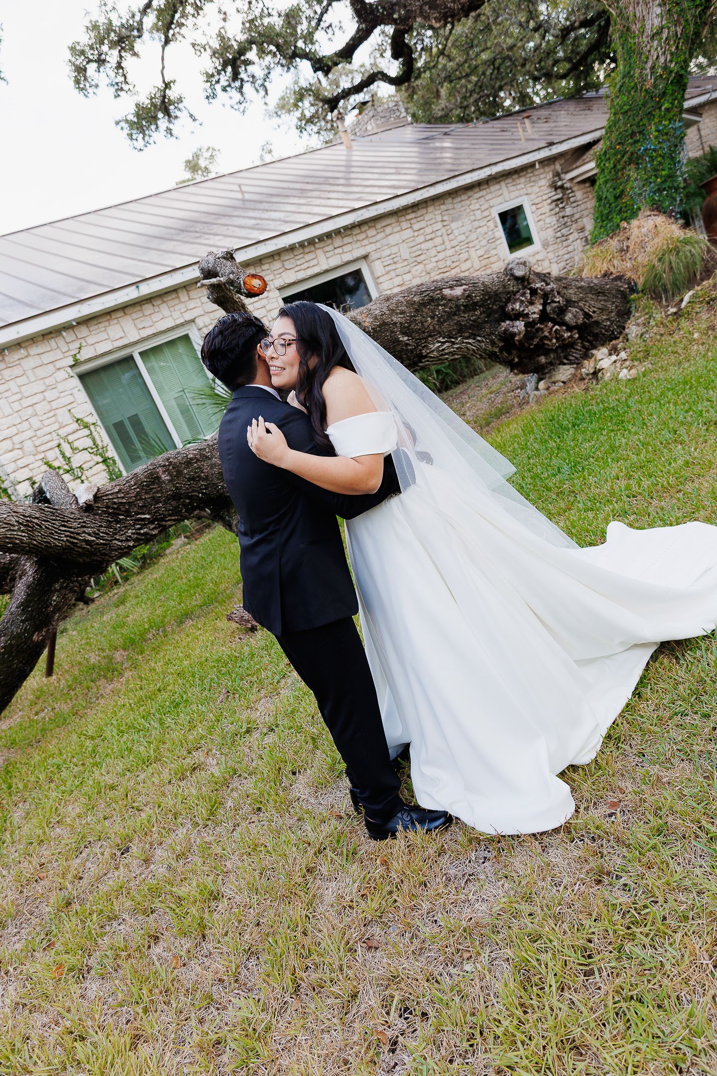 A romantic dip pose between newlyweds in formal attire on a grassy lawn with a house in the background.