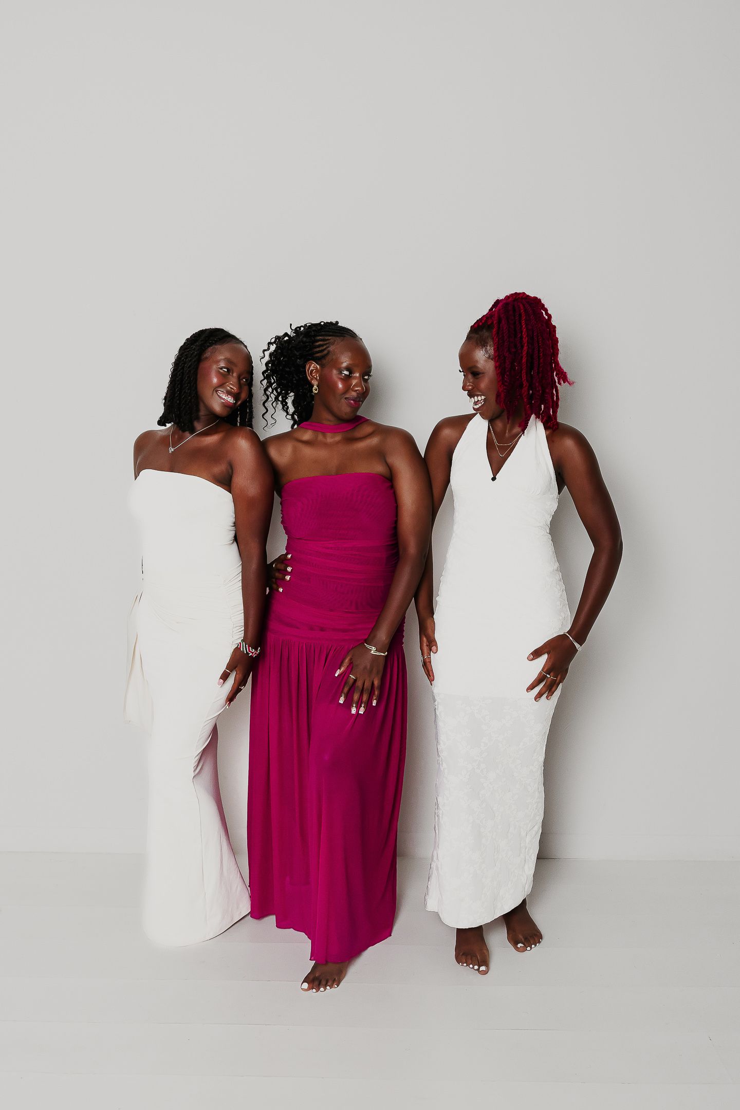Three people pose together wearing pink and white dresses against a white background in a studio setting.