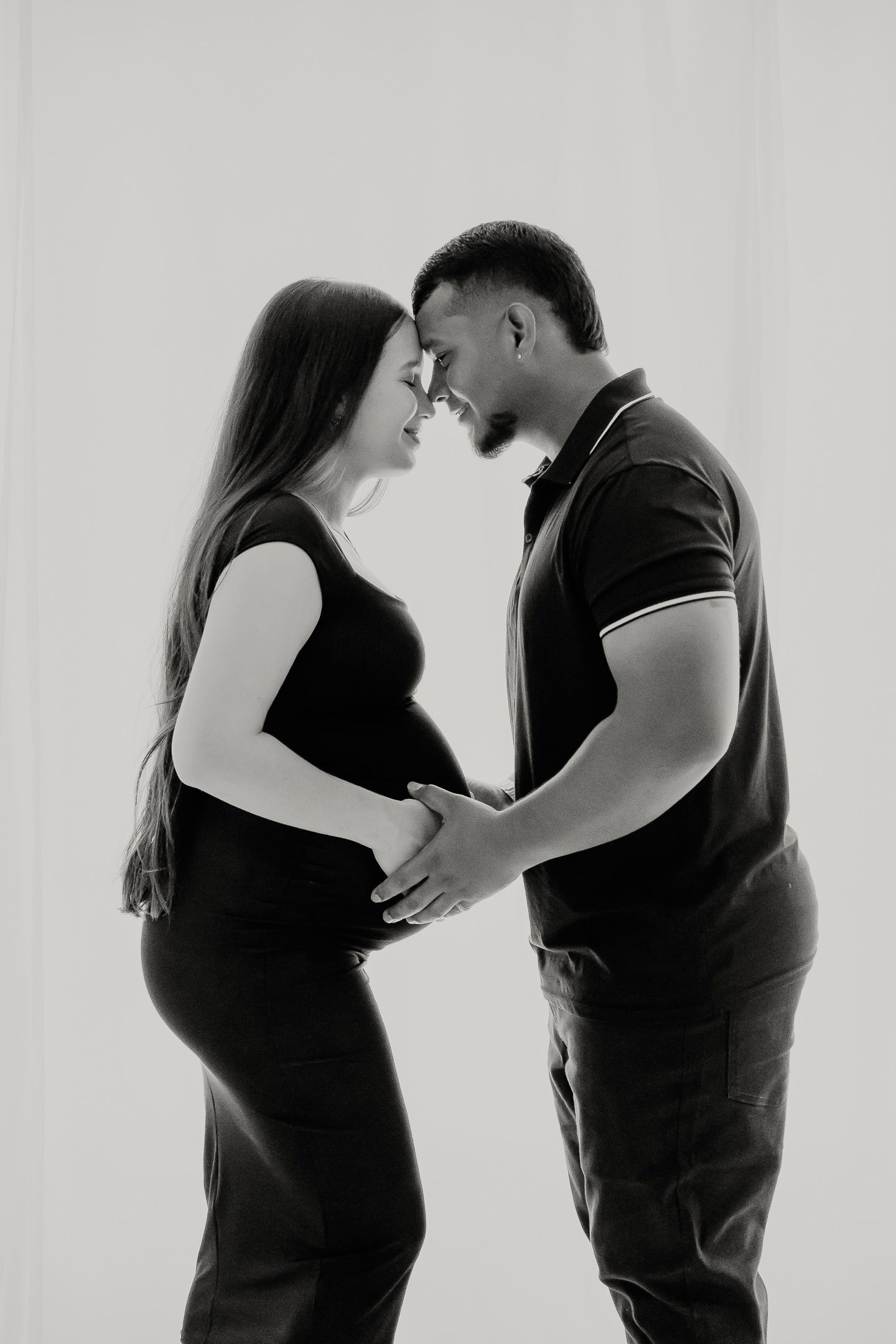 A black and white maternity photo shows an intimate moment between a couple as they share a tender embrace.