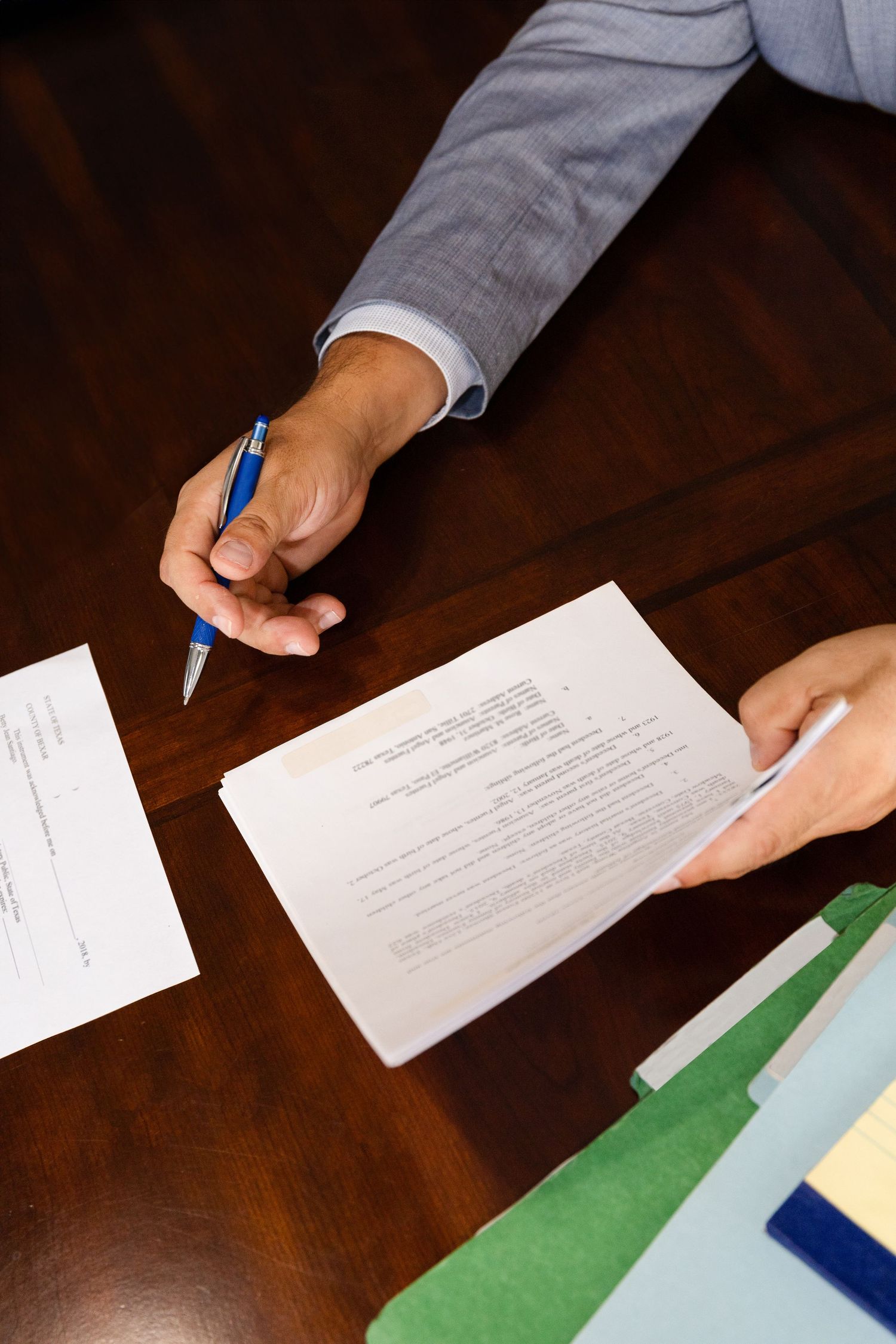 Overhead view of hands signing documents with a blue pen on a wooden desk.