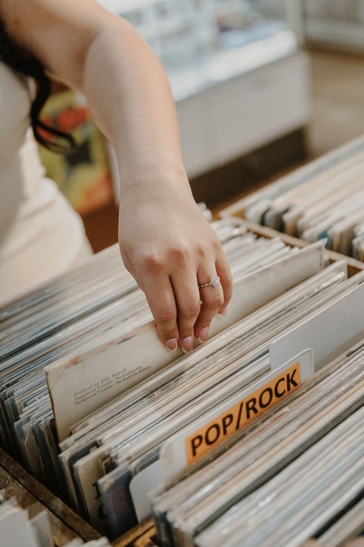 Hand browsing through vinyl records in the pop/rock section of a record store.