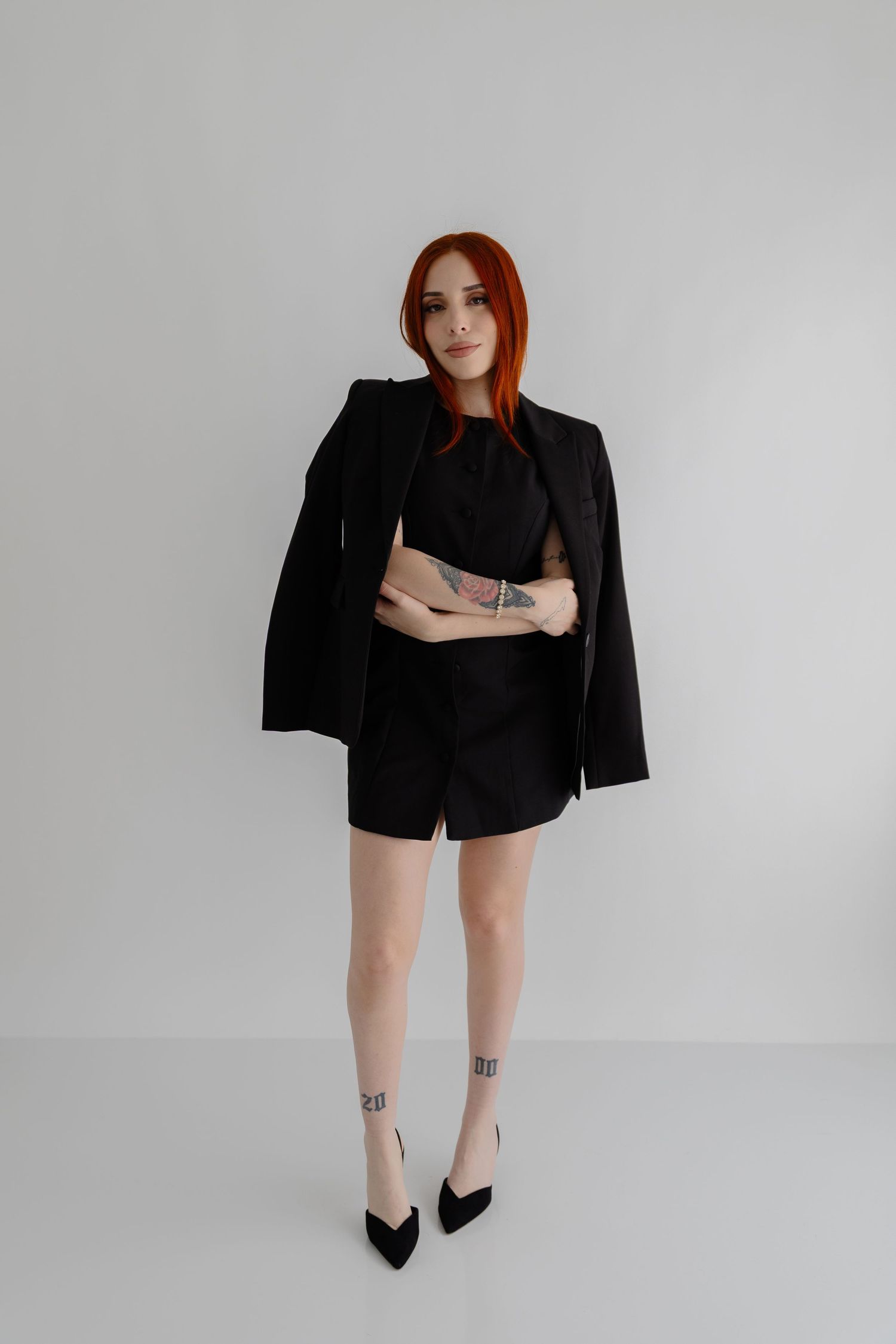 Stylish woman in black blazer and shorts poses against white background.